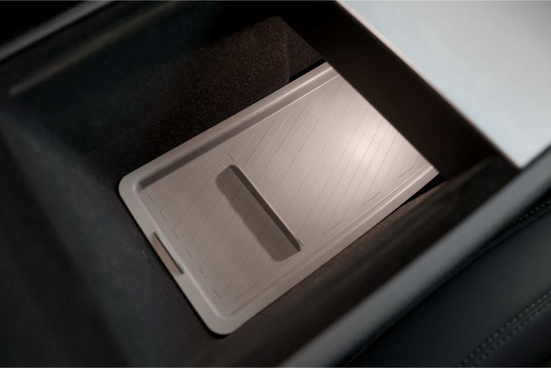 A close-up of a JOWUA Premium Interior Essentials Set – Model Y Juniper (2025+) shows the center console compartment with a textured rectangular tray insert and small handle, surrounded by sleek dark trim.