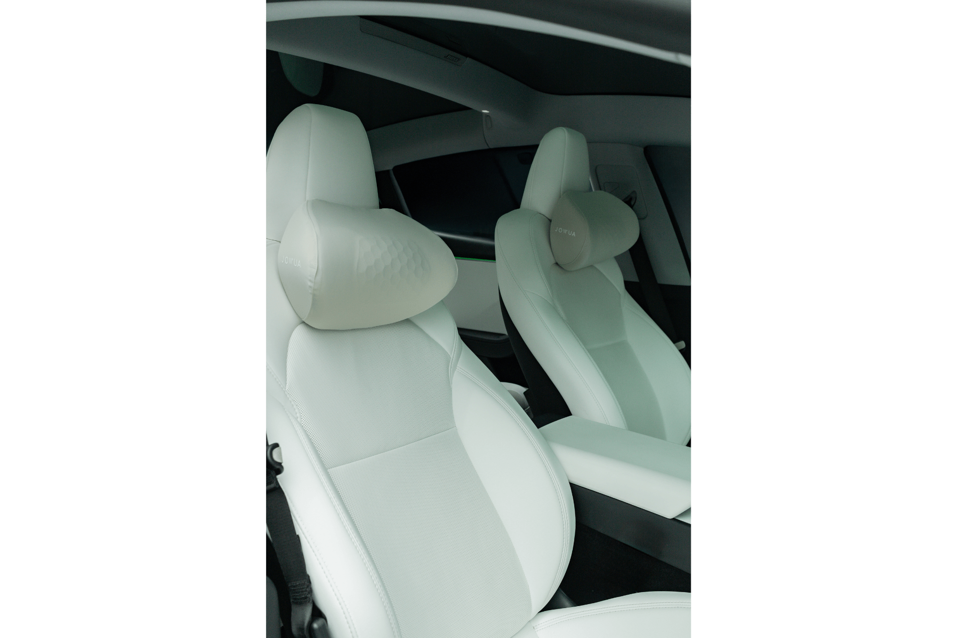 Two white, modern front car seats with headrests inside a vehicle enhanced by the JOWUA Tesla Neck Pillow, showcasing ergonomic comfort. Photo from the passenger side highlights seat details and a clean center console.