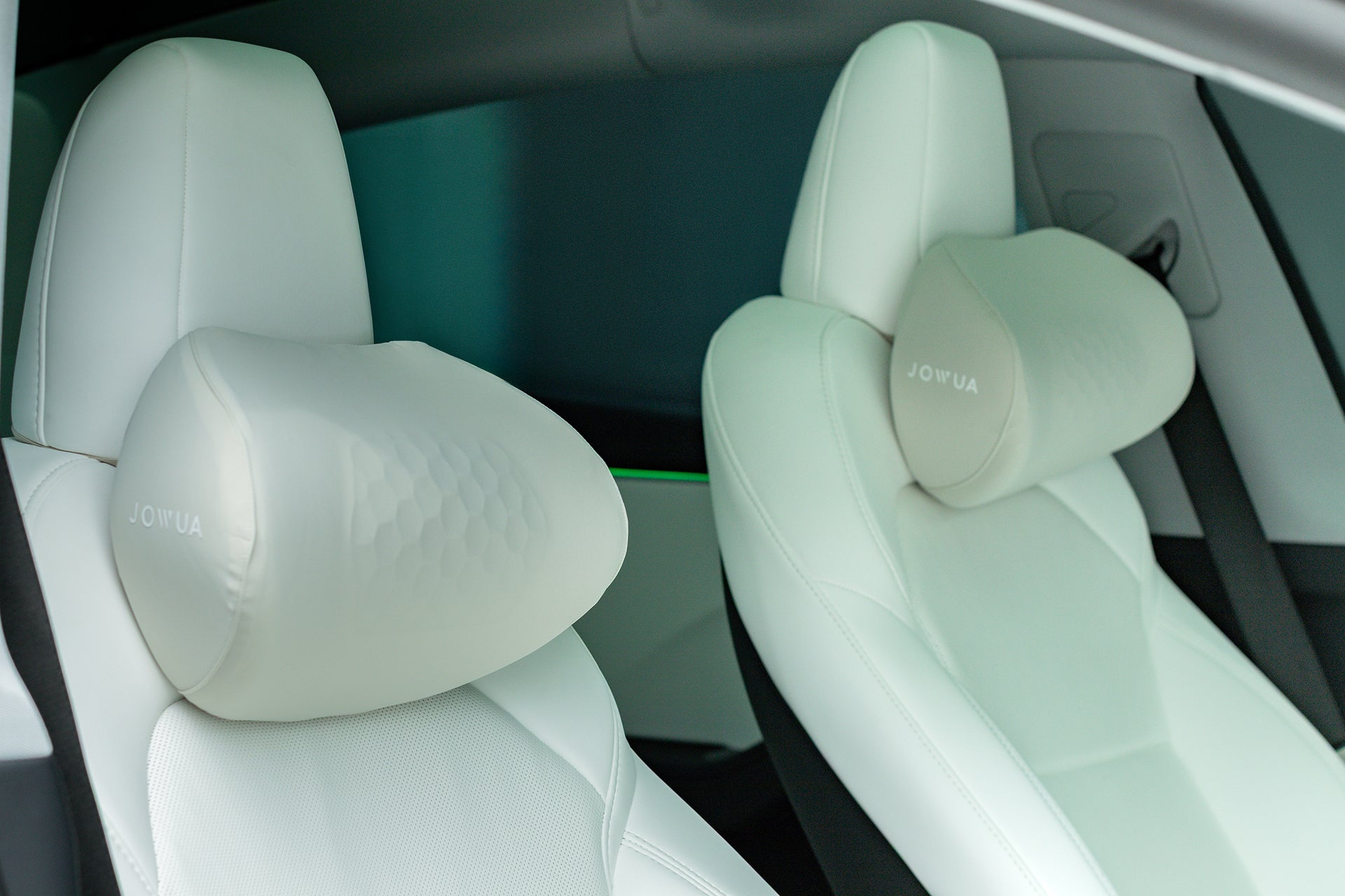 Close-up of two front white leather car seats with ergonomically designed JOWUA Tesla Neck Pillows attached for enhanced comfort. The modern, clean car interior highlights the premium look of the neck cushions.