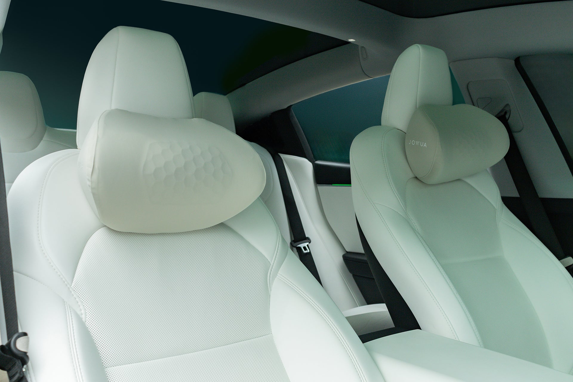 Two front car seats with white upholstery, each featuring an ergonomic design and a JOWUA Tesla Neck Pillow in a light, textured finish attached to the headrest. The modern interior appears clean and spacious.