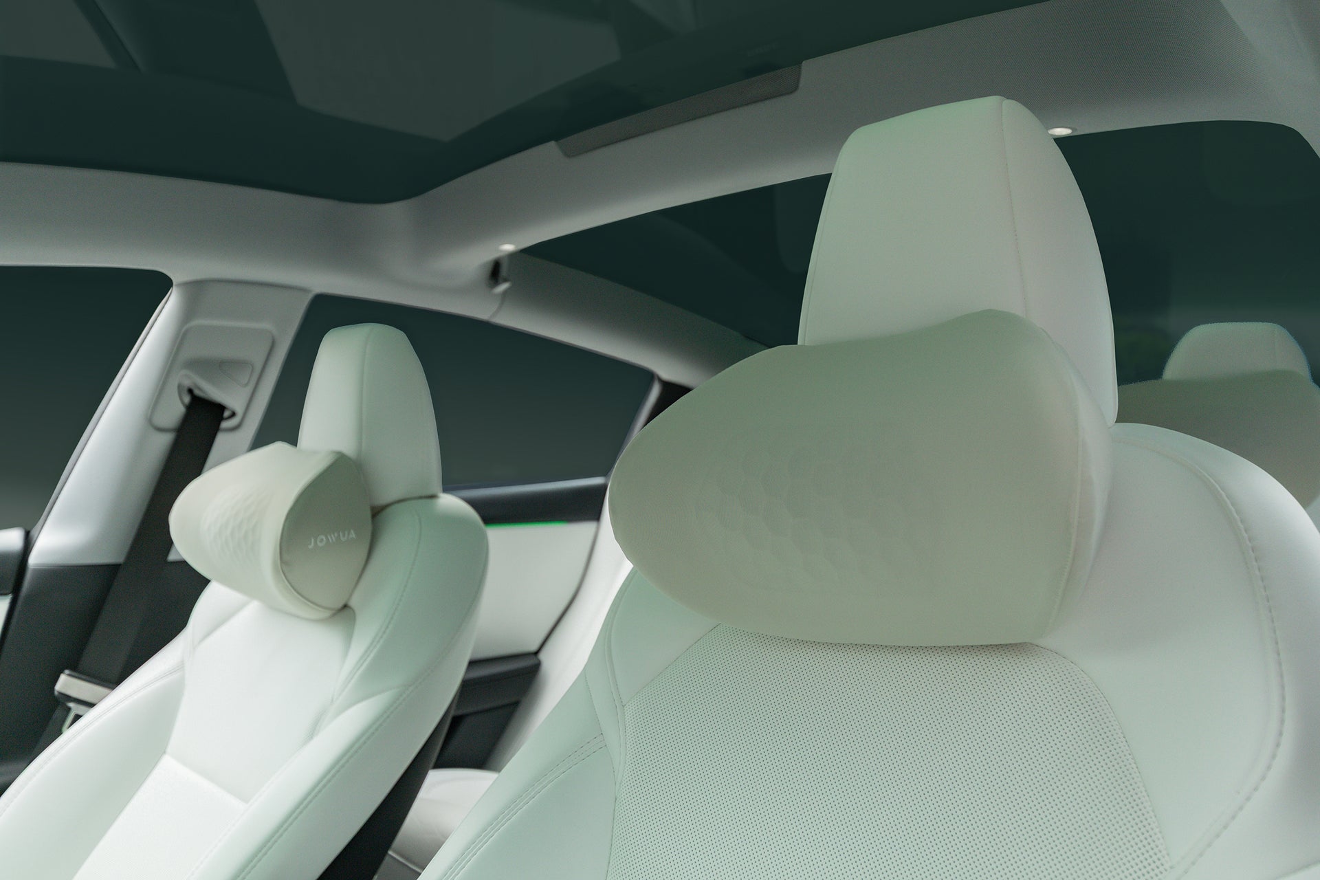 Close-up of a Tesla interior featuring JOWUA's Tesla Neck Pillow on white leather front seats with ergonomic headrests and a large glass roof, creating a clean and spacious look.