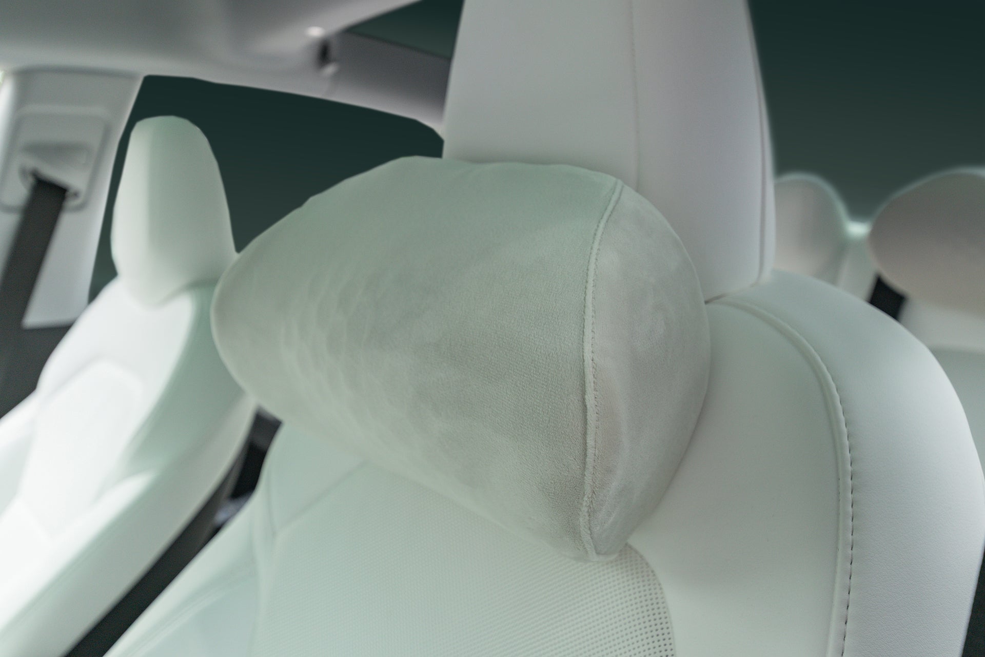 Close-up of a JOWUA Car Neck Pillow on a white car seat, showcasing its large, cushioned ergonomic headrest for neck support. Matching white seats in the background create a cohesive, modern vehicle interior.