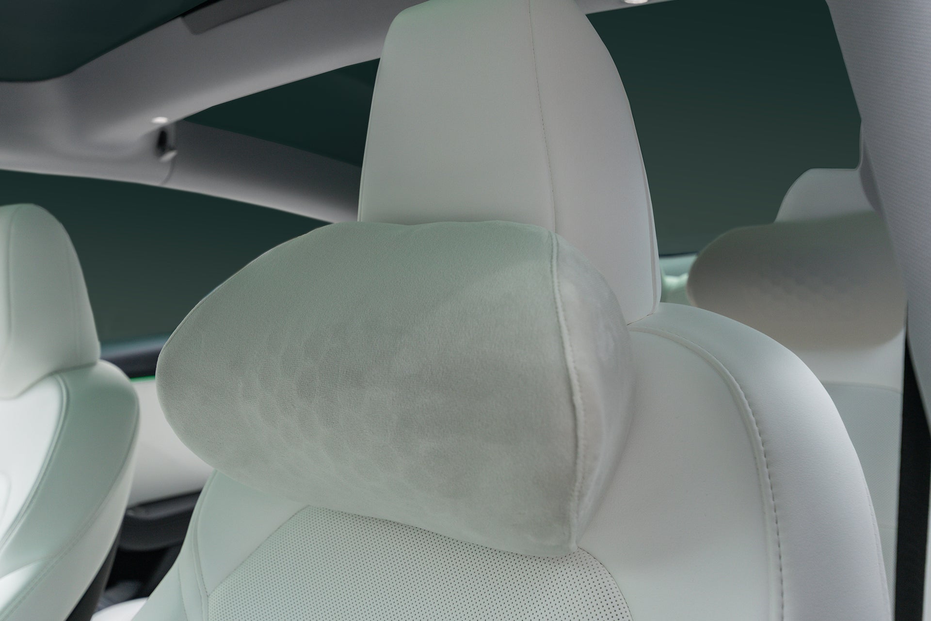Close-up of a Tesla Neck Pillow by JOWUA, in light gray plush memory foam, attached to a white car seat with smooth upholstery and ergonomic design for modern comfort inside a vehicle.