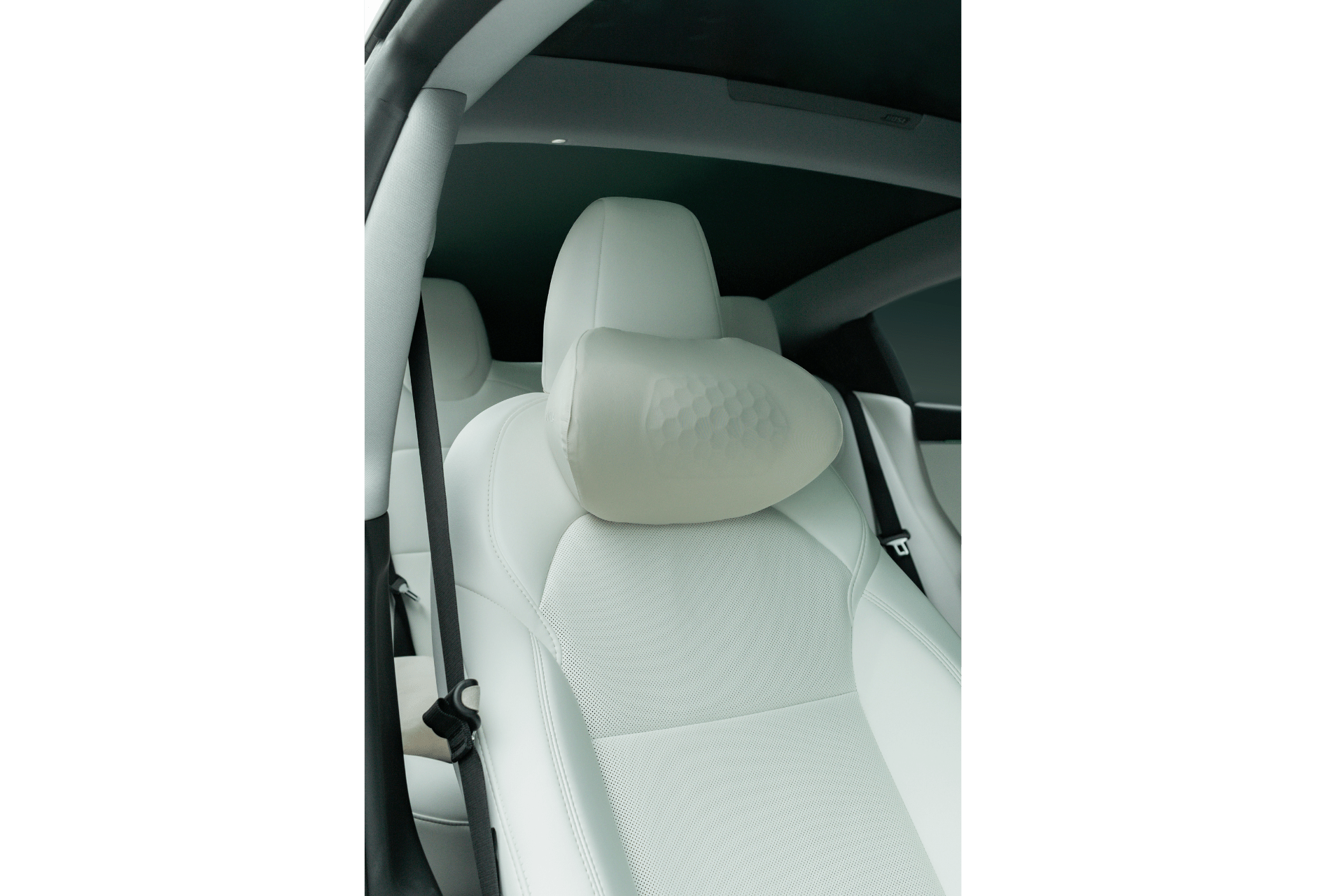 Close-up of a Tesla front seat with JOWUA's white leather neck pillow attached to the headrest, showcasing its ergonomic design and subtle geometric pattern. The seatbelt and part of the car’s interior are also visible.