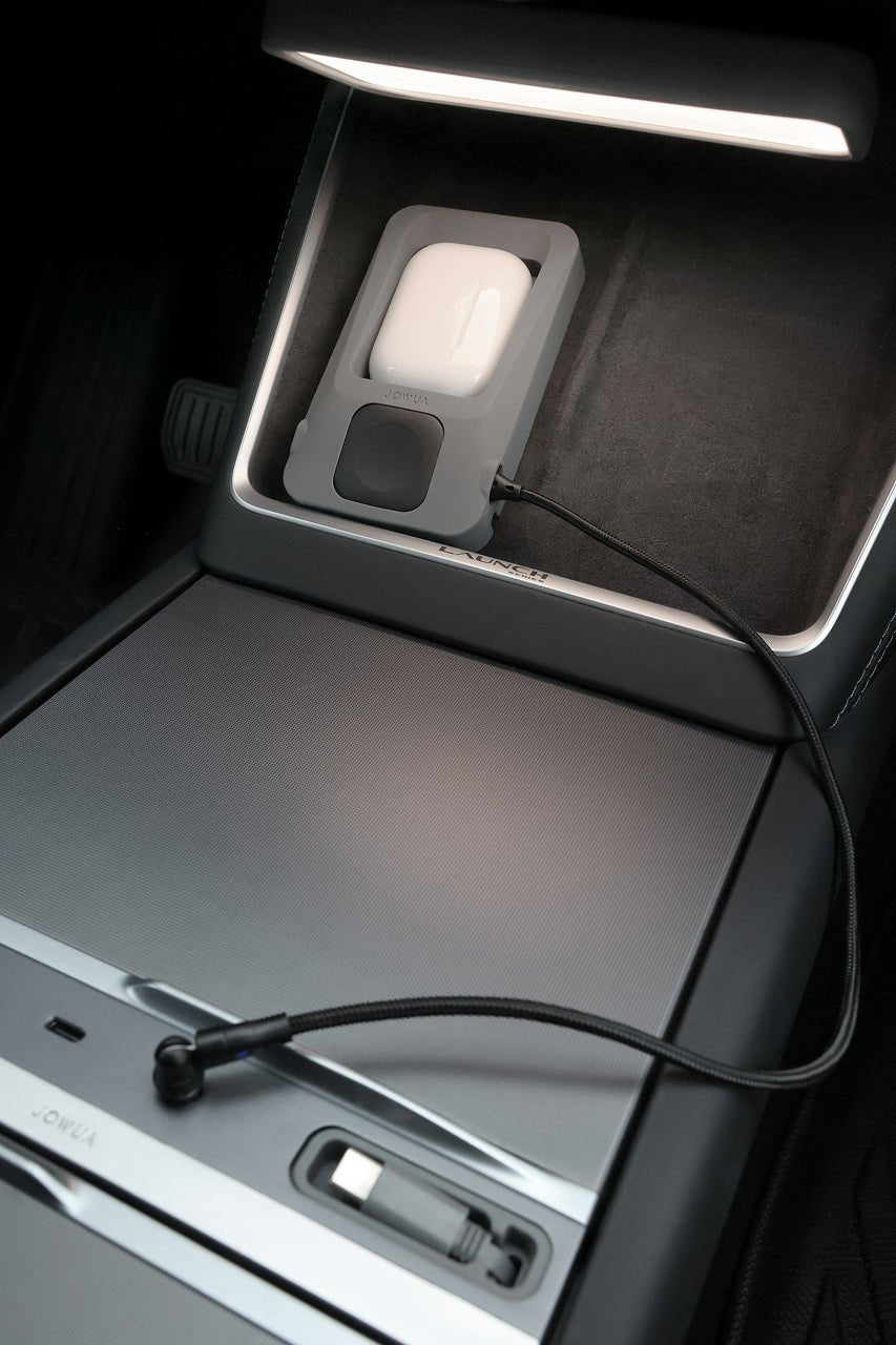 A JOWUA Power Dock Combo - Accessory Charger for Tesla is charging a white device in the car’s center console compartment, with a black USB cable plugged into the AirPods charging dock, illuminated by a built-in light.