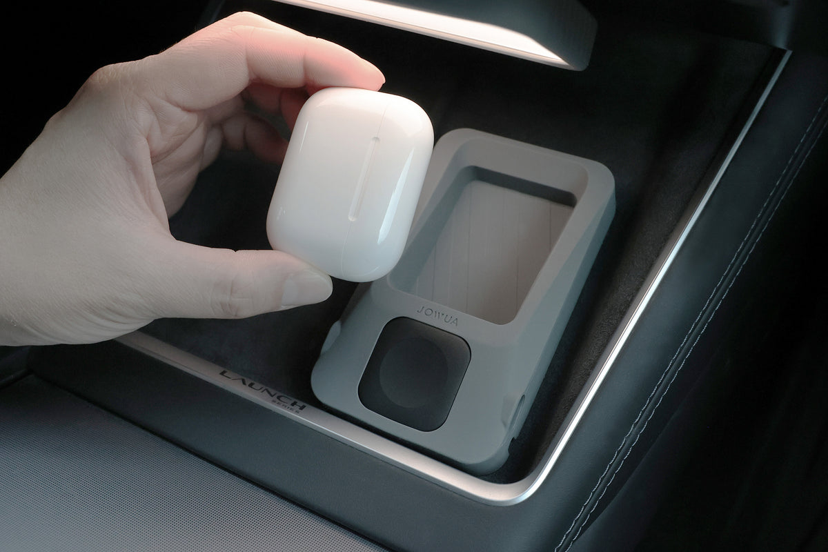 A hand holds a white wireless earbud case above the JOWUA Power Dock Combo accessory charger, elegantly positioned on the Tesla center console.