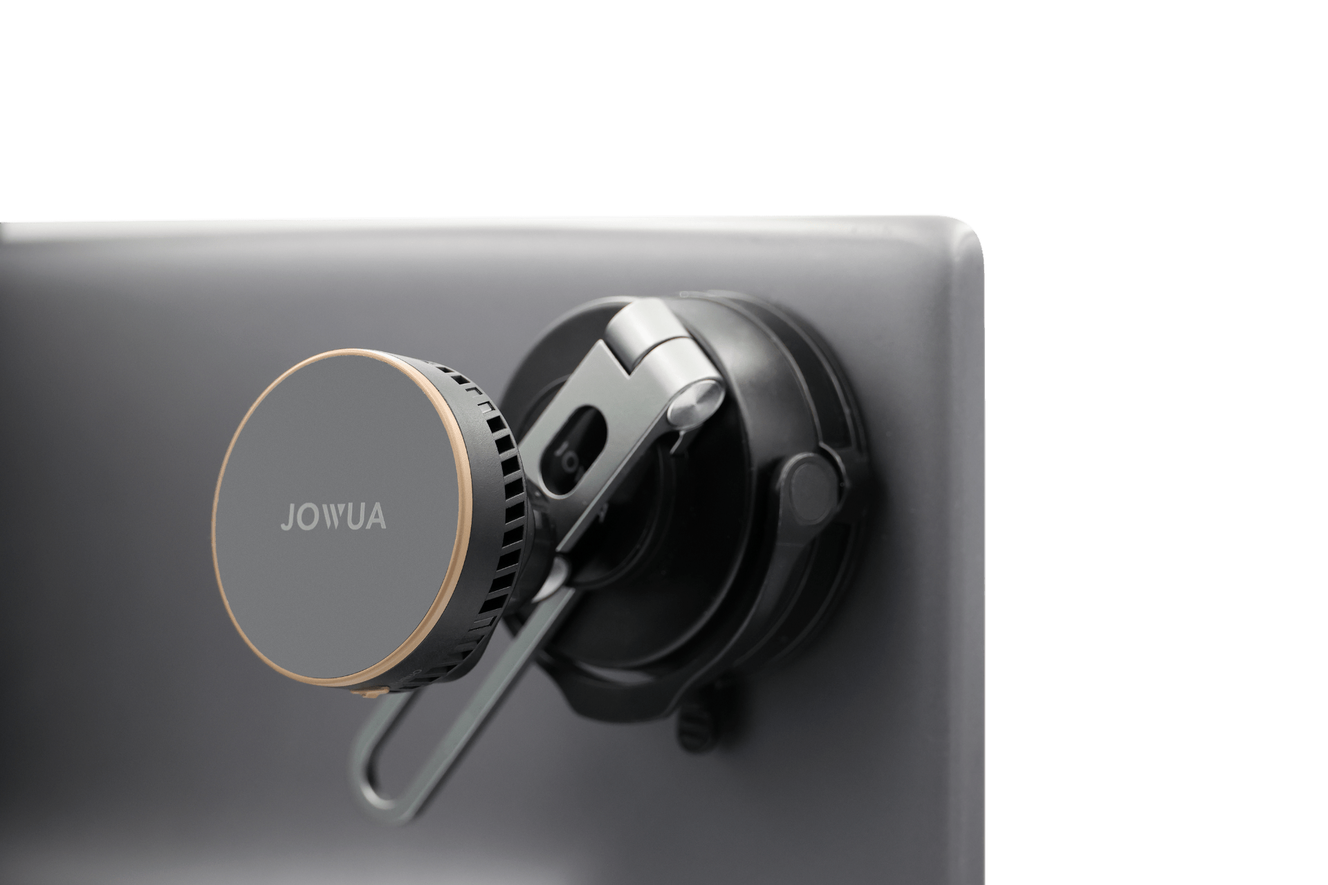 A close-up of a JOWUA Active Cooling Tesla Compatible Phone Mount with a gold-edged circular design, Qi2 wireless charging, attached to a monitor or flat surface using its suction mount and adjustable clip.