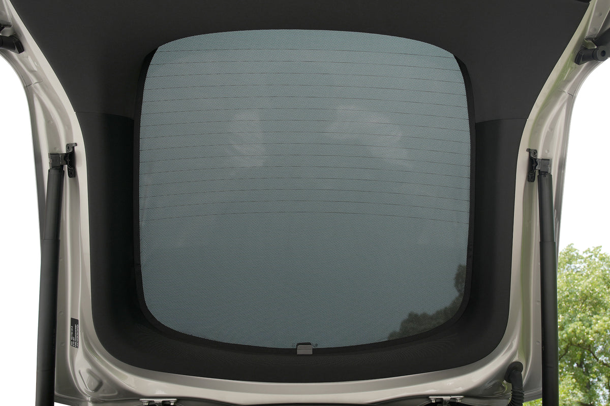 View from inside an open car trunk looking up at the rear window, where the JOWUA Rear Lift Gate + Triangular Window Sunshade for Model Y L (2026+) is installed. The custom-fit sunshade covers the rear glass while still allowing a clear view outside, effectively blocking heat from entering through the rear window; part of the car frame and some trees and sky are visible through the shaded glass.