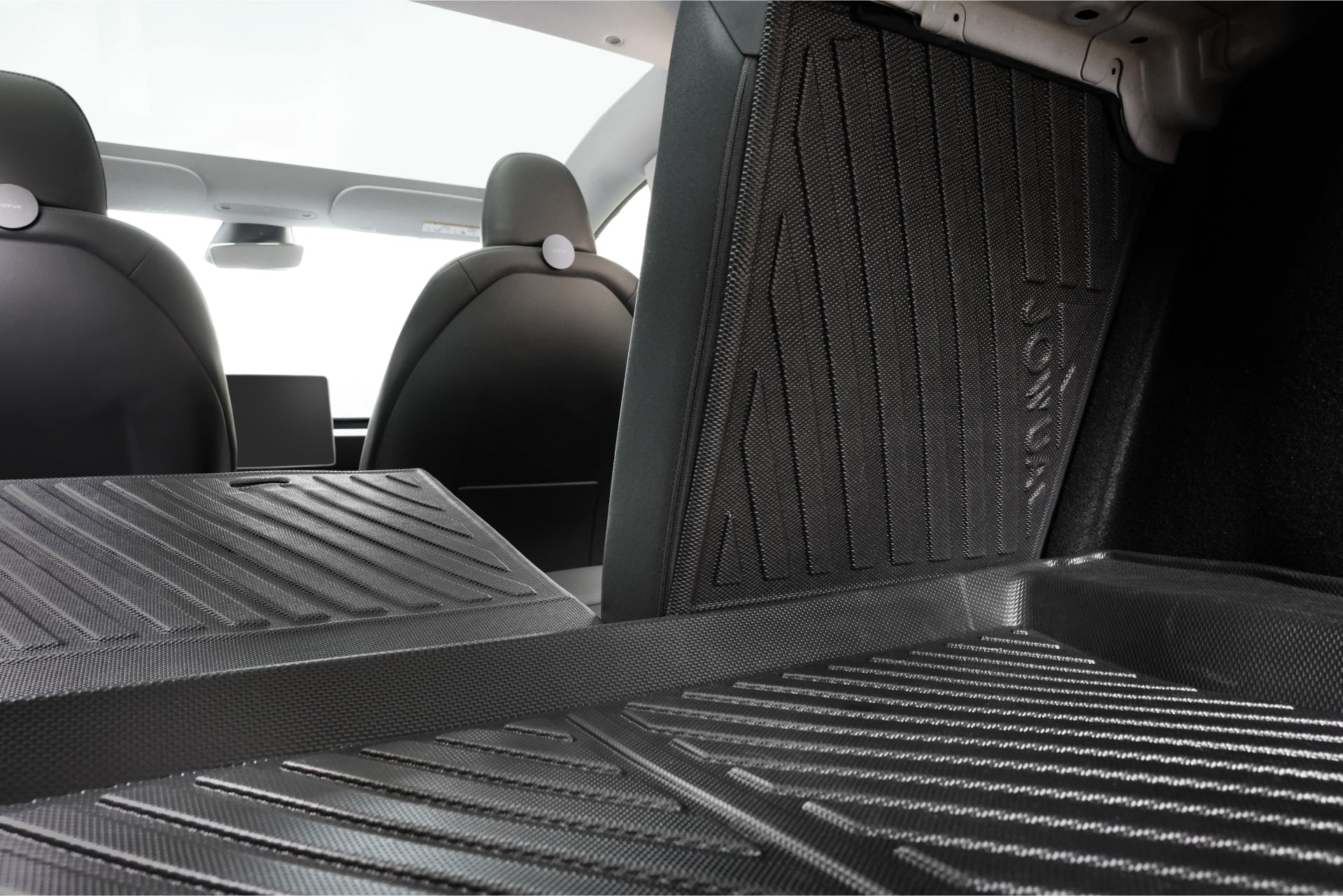 Close-up of the rear cargo area featuring the JOWUA Model 3 All Weather Trunk Combo (Model 3 Highland, 2024+) with black rubber mats; front seat backs and dashboard touchscreen appear in the background.