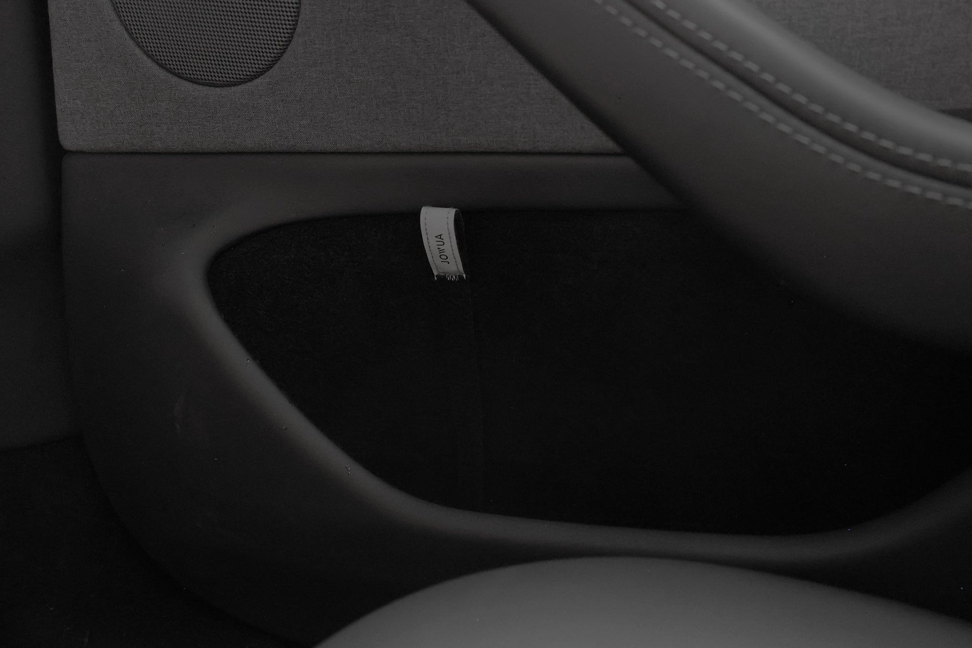 Close-up of a Model 3 Highland/Model Y interior rear door, featuring the JOWUA Reflective Rear Door Emergency Release Strap and injection-molded hook design, with part of the door handle, speaker, and "SRS AIRBAG" tag visible.