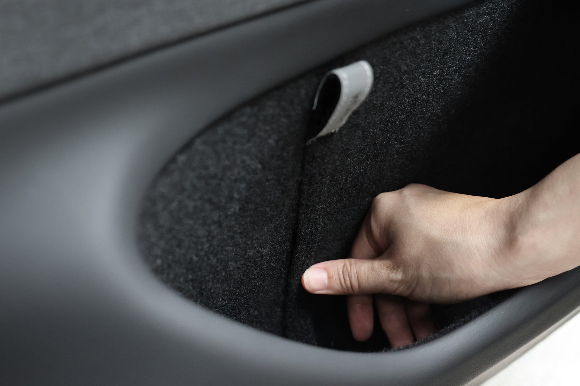 A hand pulls a JOWUA Reflective Rear Door Emergency Release Strap from a fabric-lined car door compartment—an essential accessory for safety and convenience in the Model 3 Highland (2024+) and all Model Y vehicles.
