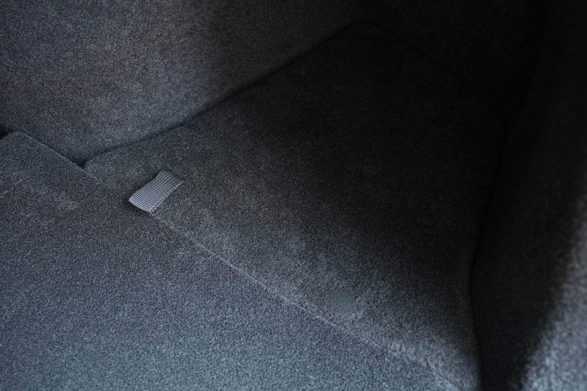 Close-up of a Tesla Model Y L (2026+) trunk interior, highlighting the clean dark gray carpet and a convenient fabric loop tab on the floor—ideal for accessing your hidden JOWUA Trunk Storage Bins + Ambient Light Bundle or organizing essentials with silicone organizers.