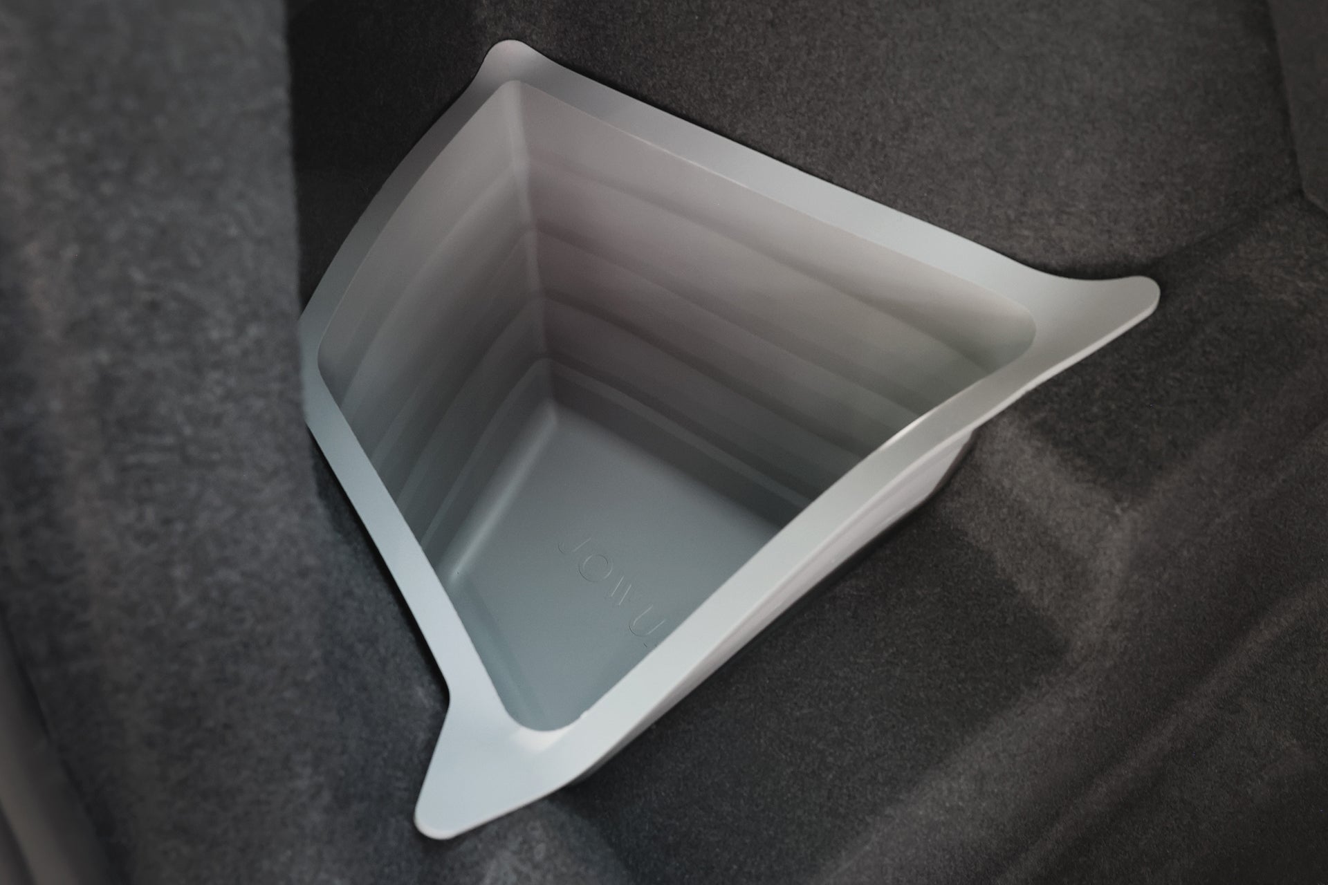 A JOWUA Trunk Storage Bins Bundle for Model Y (Juniper 2025+) in gray, featuring collapsible angled sides, is placed in the corner of a trunk with dark carpet.