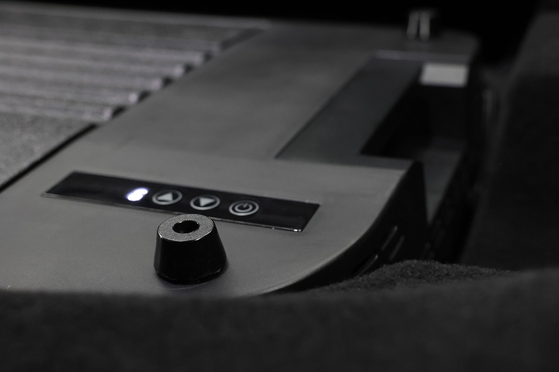 Close-up of JOWUA Car Refrigerator for Tesla Model Y’s black control panel with play, pause, and power touch buttons. A small cylindrical object sits in the foreground. This model features intelligent dual-mode cooling for enhanced performance.