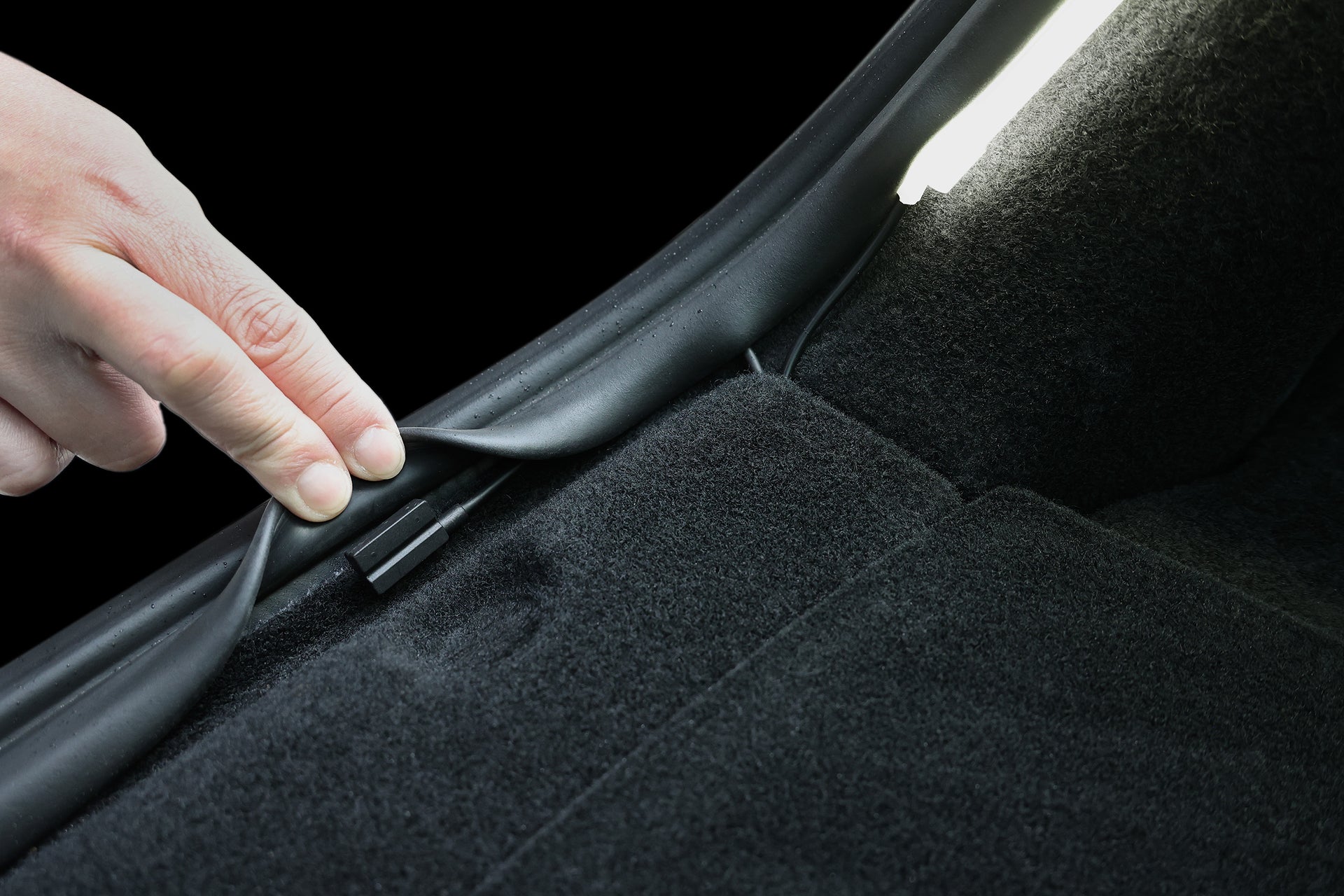 A close-up of a hand pulling back a black rubber seal in the Tesla Model Y trunk reveals a clip underneath—making it easy to install the JOWUA Teslussy Light > Type-C Ambient Light & 3 in 1 Car Charger for enhanced lighting and charging.