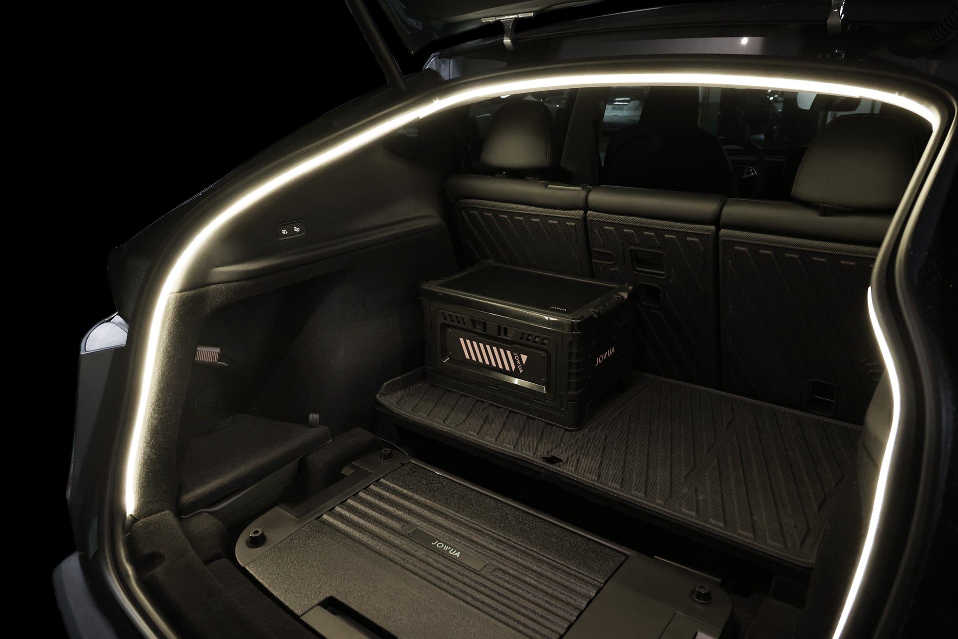 Open the Tesla Model Y trunk to reveal JOWUA's USB-C LED Strip Ambient Light, automatically illuminating a black foldable storage box on the floor, while rear seats are visible in the background.