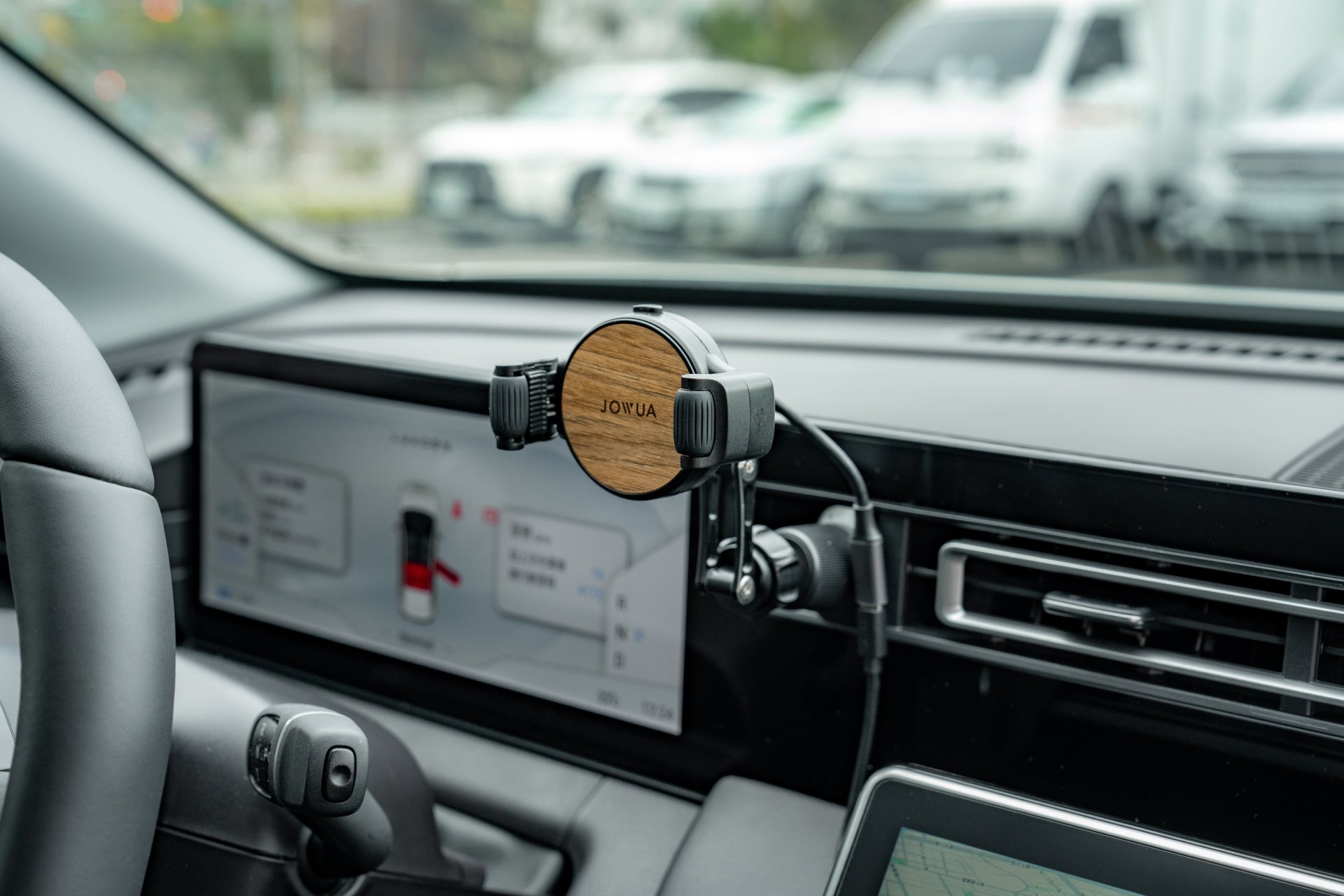 A JOWUA Universal Air Vent Car Mount (Qi2 Universal Roller Mount) is attached near the infotainment screen with a phone displaying navigation. Several cars are visible through the windshield in the background.