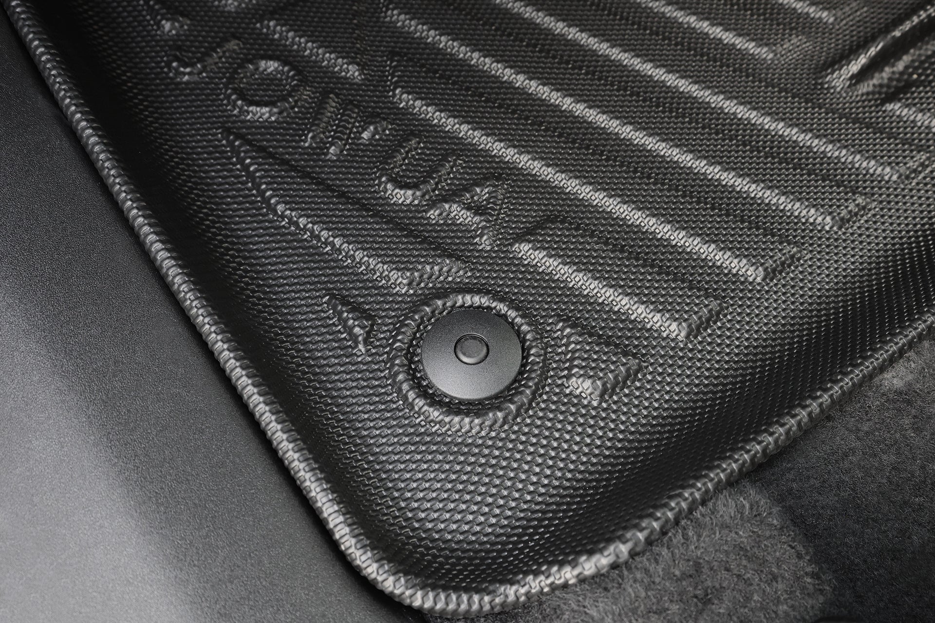 Close-up of the JOWUA All Weather Floor Liner for Volvo EX30, showing a textured black custom fit mat with a circular fastening button, raised ridges, and partial coverage of the car’s dark carpeted floor.