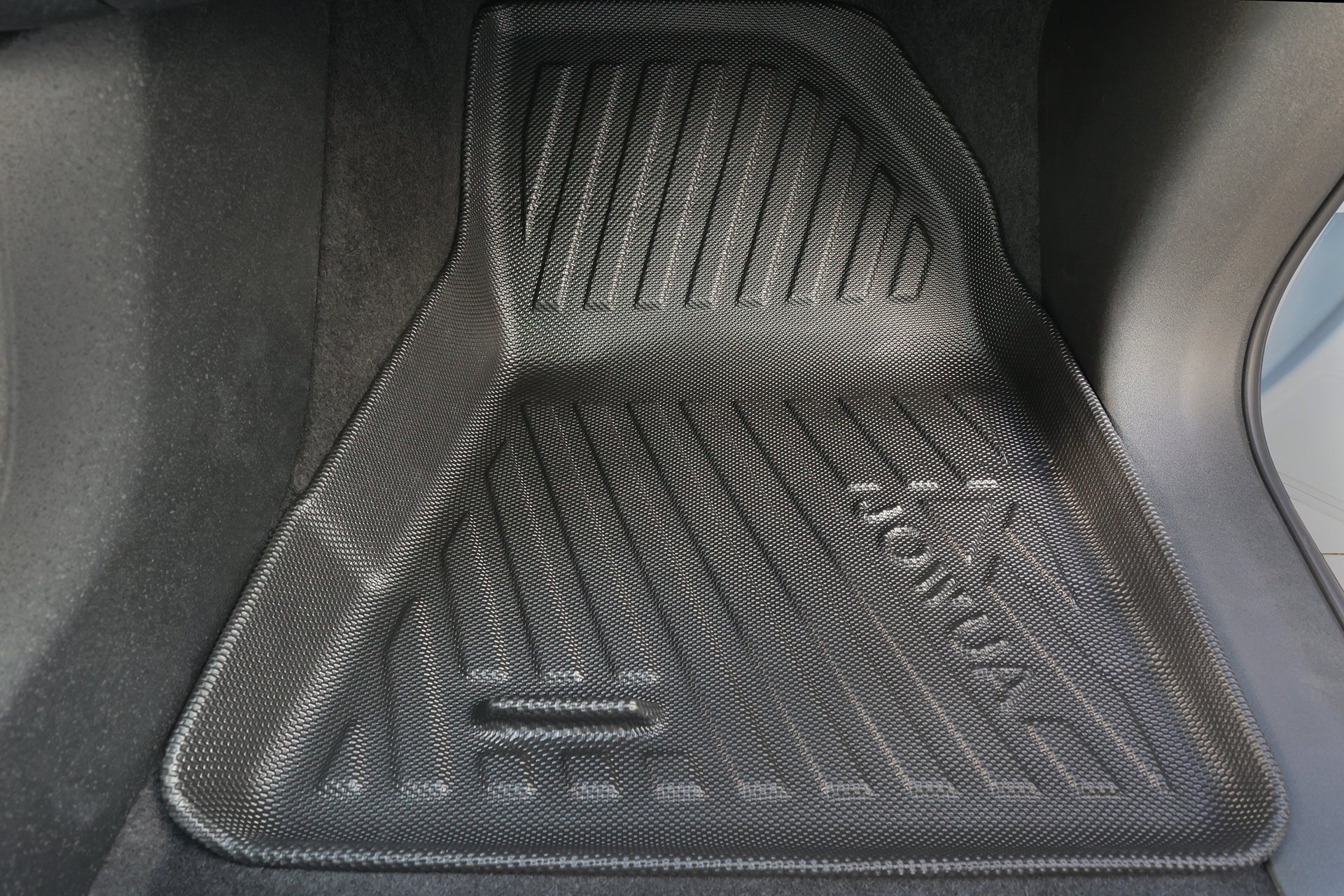 Close-up of a black, textured JOWUA All Weather Floor Liner for Volvo EX30 with raised edges and custom fit, tightly installed in the car’s footwell area.