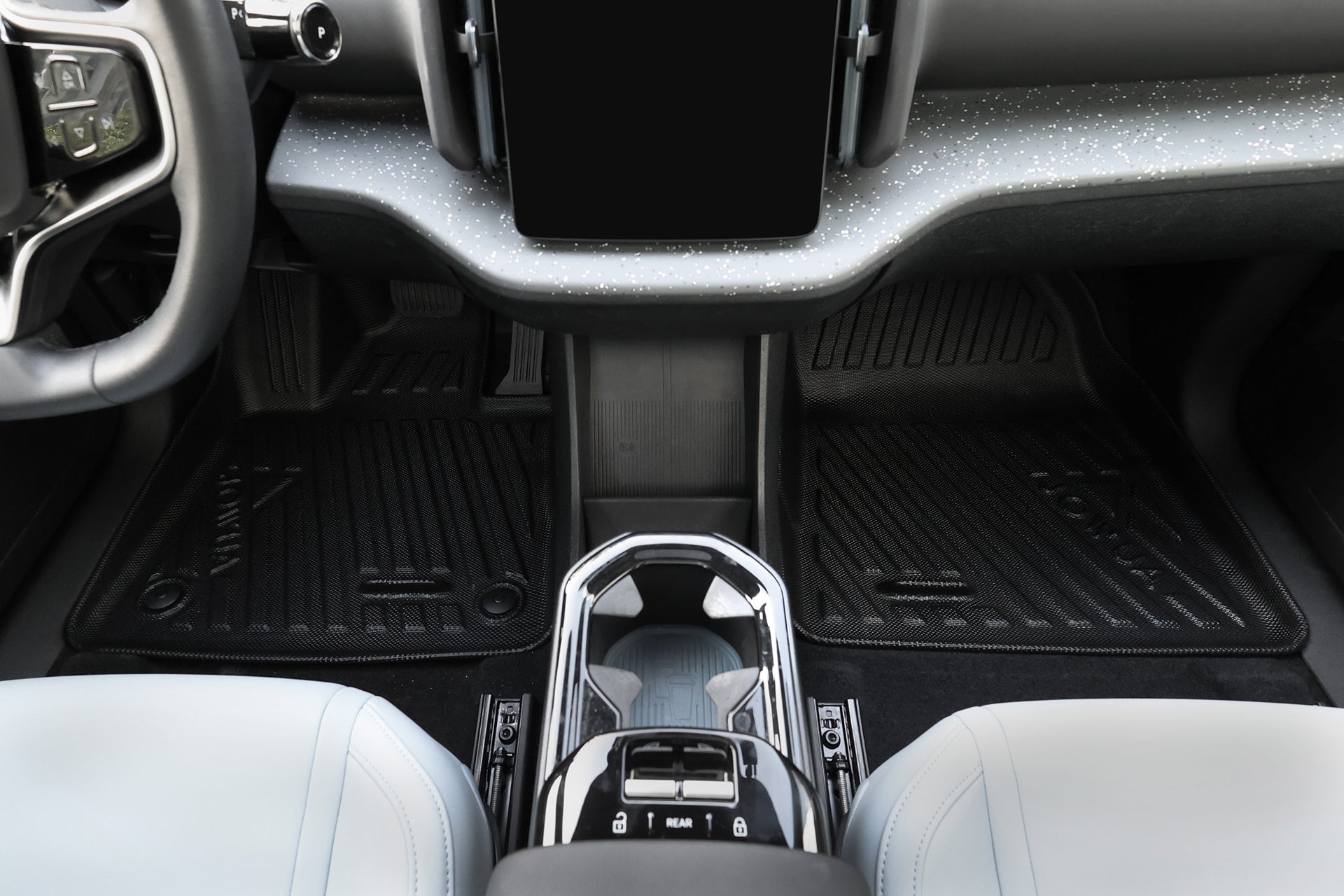 View of a car’s front interior with the center console, gear selector, two light-colored seats, touchscreen display, and a black JOWUA All Weather Floor Liner (Volvo EX30) custom fit for the vehicle.