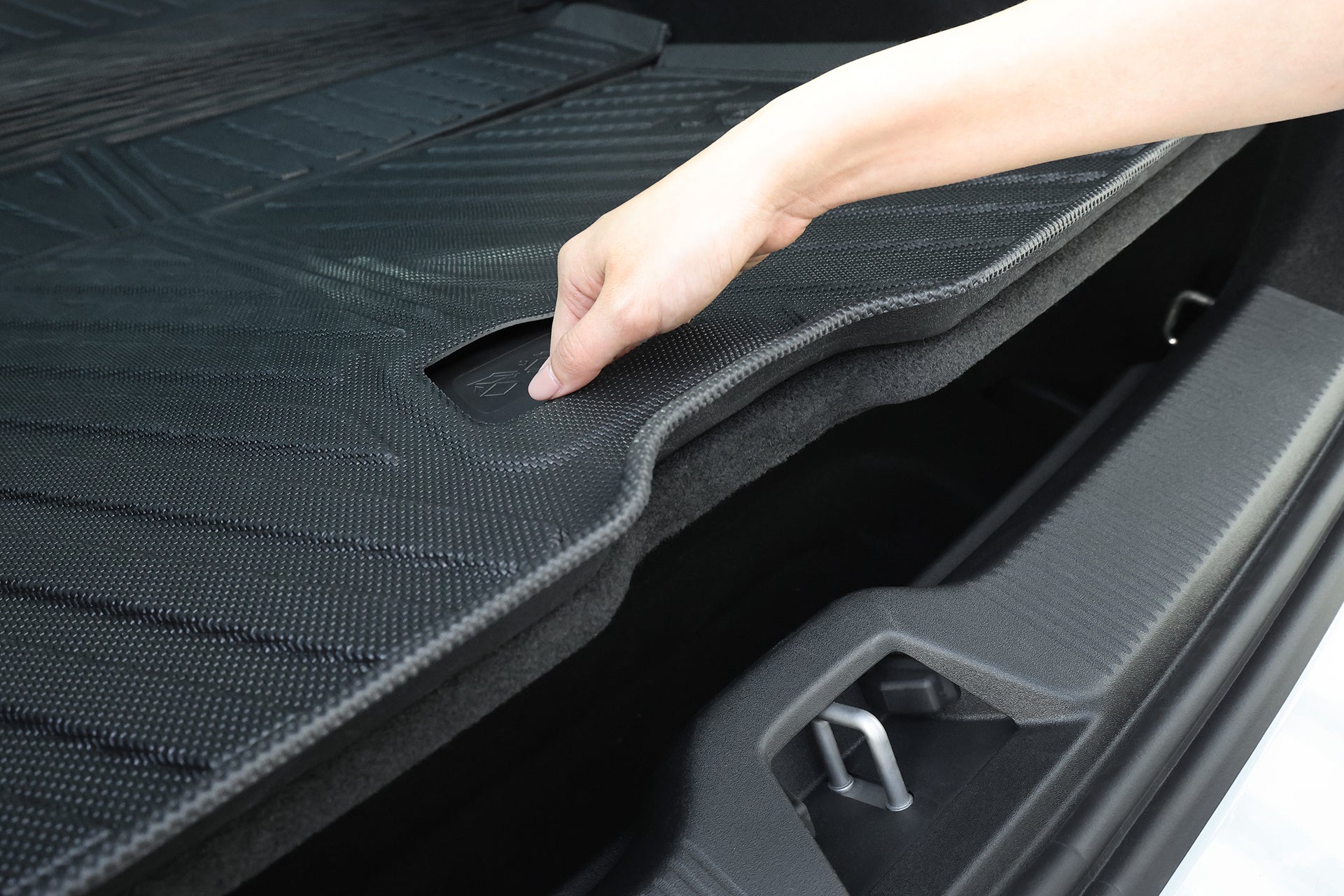 A hand lifts the JOWUA All Weather Trunk Liner + Rear Seat Cover (Volvo EX30) in a vehicle's trunk, revealing a handle and hidden storage compartment underneath.