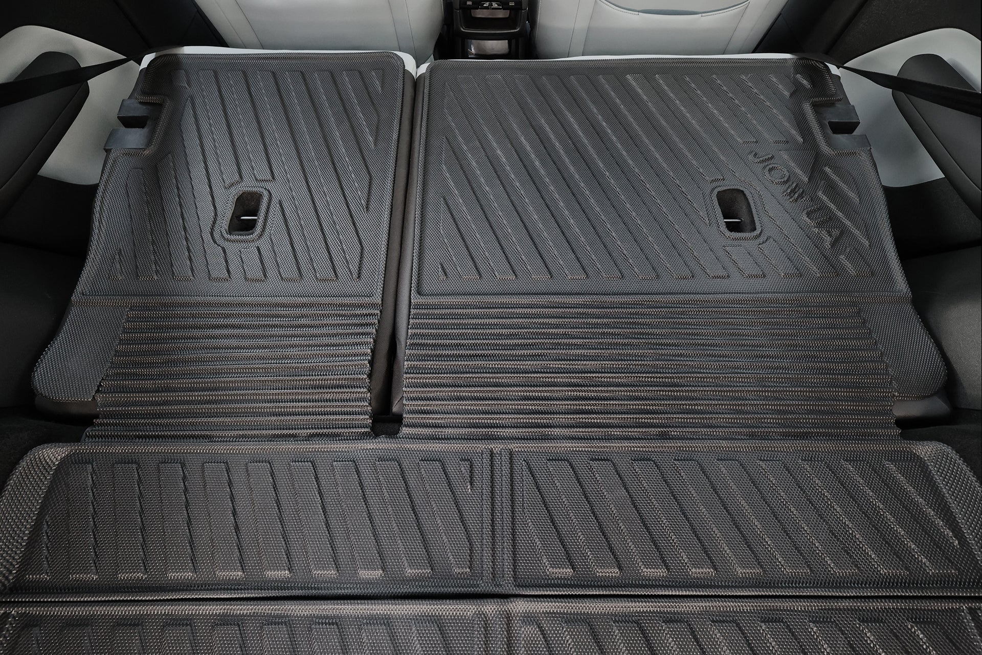 Close-up of rear seats folded flat in a Volvo EX30, covered by the JOWUA All Weather Trunk Liner + Rear Seat Cover. The black mat protects the extended cargo area, with seatbelts and car doors visible on the sides.