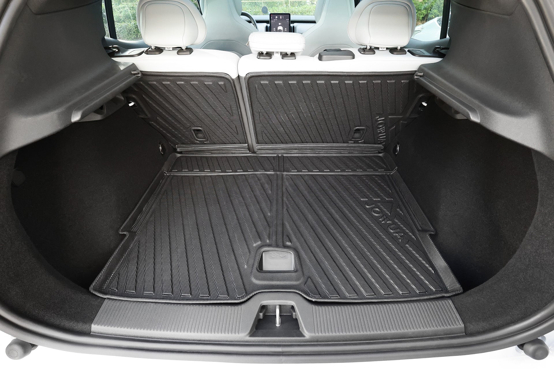 The image displays the spacious cargo area of a Volvo EX30 with rear seats upright, protected by JOWUA’s All Weather Trunk Liner + Rear Seat Cover. White headrests and a digital display complete the modern interior.