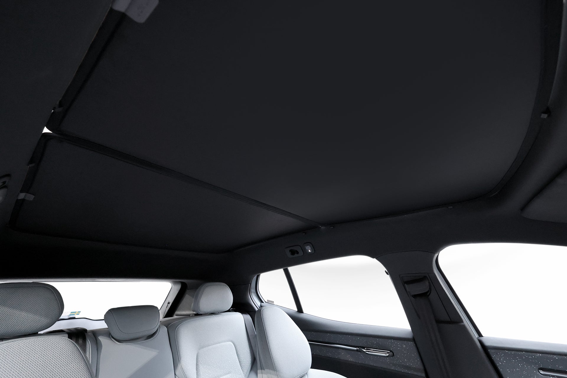 View from the back seat of a Volvo EX30 with light gray mesh fabric seats and a large closed panoramic sunroof, equipped with the JOWUA Glass Roof Sunshade for extra UV protection and comfortable bright interior.