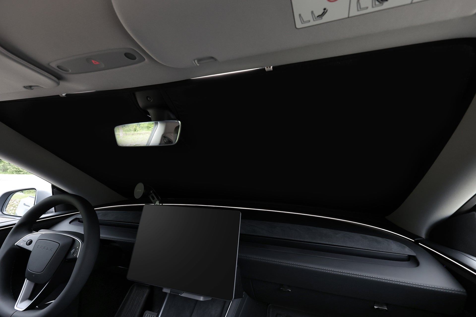 Inside a modern car, the JOWUA Windshield Sunshade for Model Y Juniper (2025+) covers the windshield, providing UV protection and blocking the outside view. A large touchscreen display, steering wheel, and rearview mirror are visible.