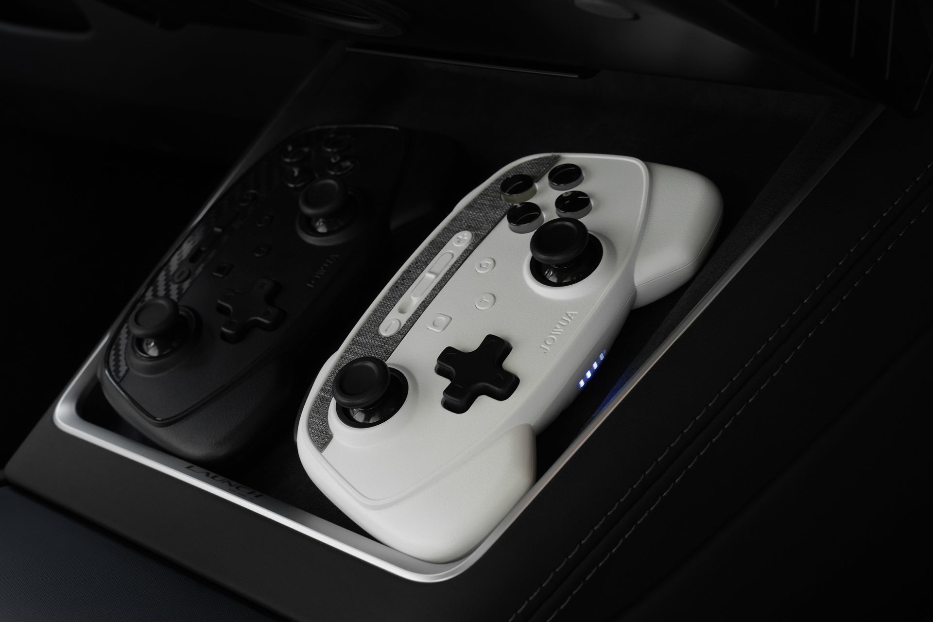 Two JOWUA Wireless Tesla Game Controllers (Model S/X/3HL/Y Juniper/Cybertruck), black and white, rest in a sleek compartment. The white controller’s blue lights highlight Bluetooth connectivity and multi-platform gaming support.