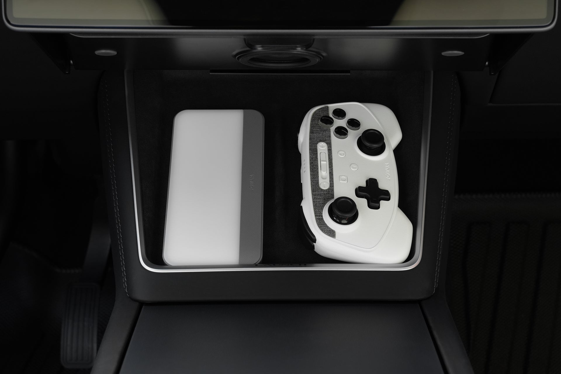 A JOWUA Wireless Tesla Game Controllers Combo and a closed silver case are placed side by side inside a car’s center console storage compartment.