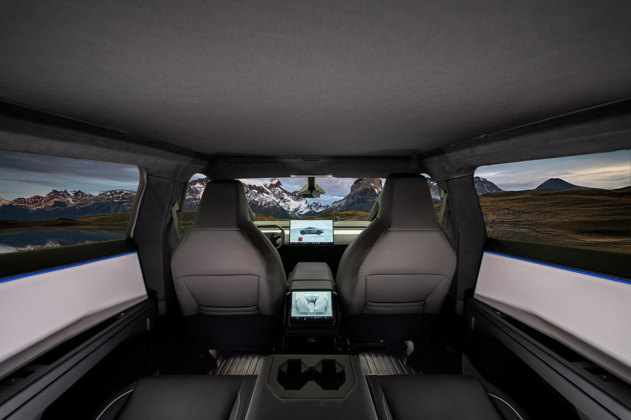 Rear-seat view in a Cybertruck with JOWUA’s Glass Roof Sunshade, featuring mesh UV protection, two front seats, large dashboard screens, and windows framing a mountain landscape beneath cloudy skies.