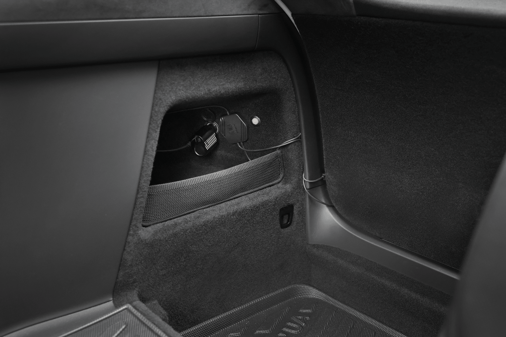 A close-up of a Tesla Model X trunk shows a JOWUA Tesla Model X Trunk Ambient Light—USB-C LED Strip—illuminating the rear interior, highlighting a small storage compartment with charging cable, dark carpeting, and plastic trim.