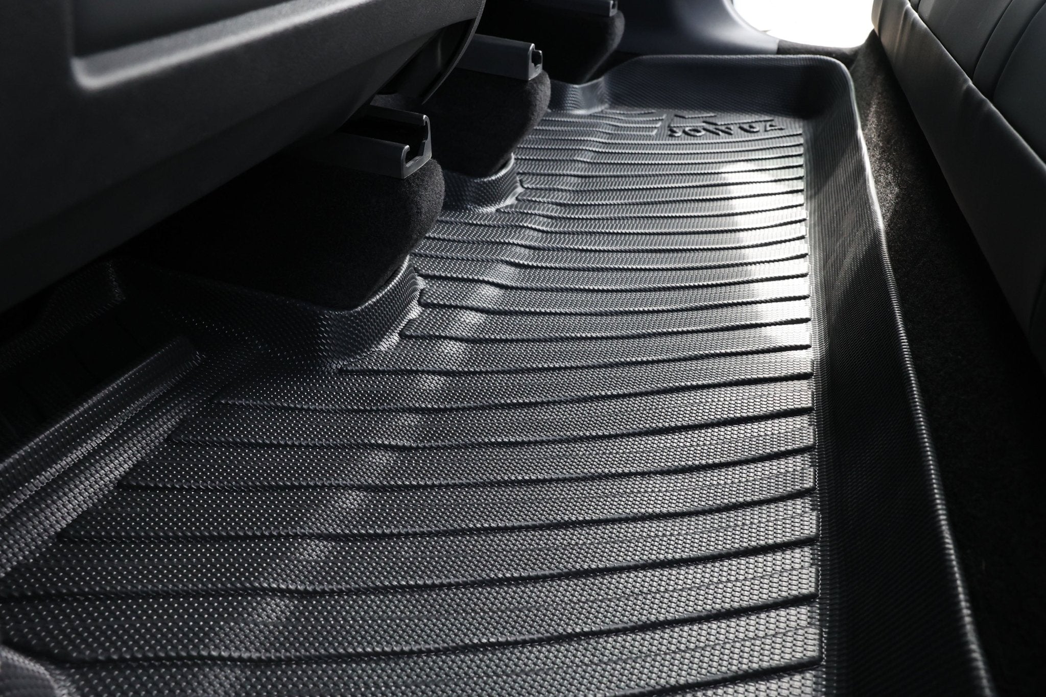 Close-up of a black, textured car floor mat from the JOWUA Premium Interior Essentials Set (RHD) – Model Y Juniper (2025+), covering the rear seat footwell with contoured ridges to trap dirt—an essential upgrade for your Tesla's interior.