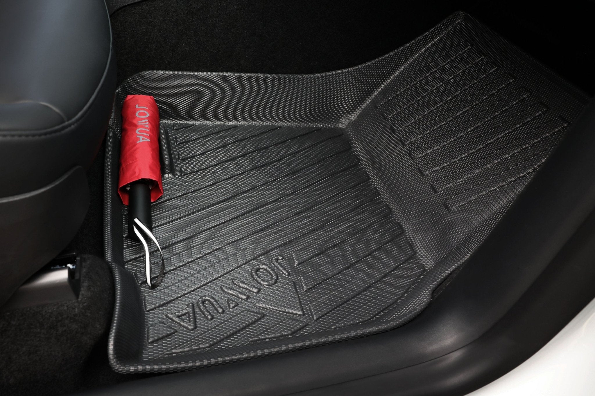 A close-up of a JOWUA car floor mat embossed with "JOLYVA," and a red umbrella with curved handle—part of the Premium Interior Essentials Set – Model Y Juniper (2025+)—a sleek upgrade for your Tesla's interior.