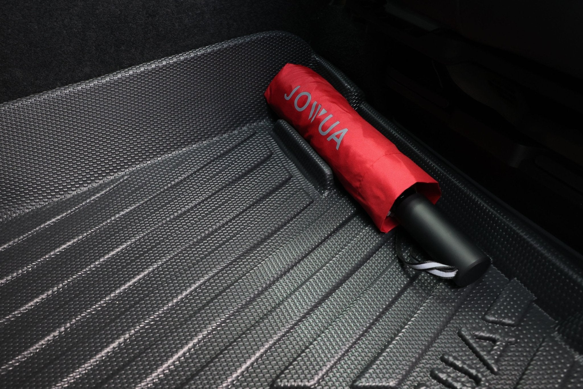 A closed red JOWUA umbrella rests on Model Y All-Weather Floor Liners Combo - Juniper Compatible (Right Hand Drive Version), the perfect Tesla Model Y accessory.
