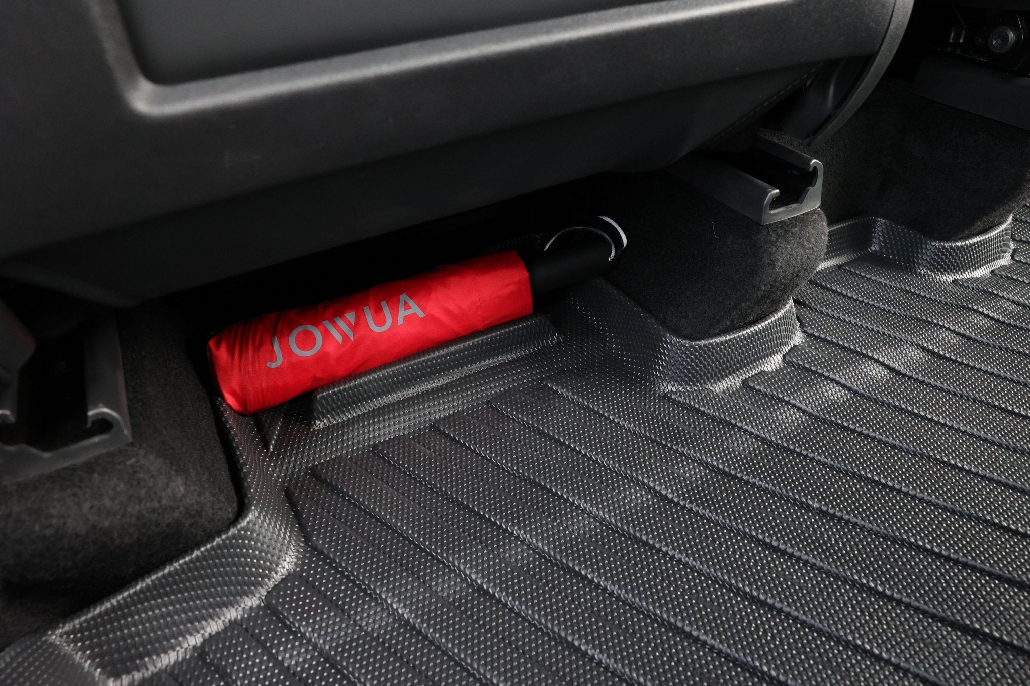 A red umbrella with "JOWUA" written on it is stored under a car seat on Model Y (Juniper 2025+) All-Weather Floor Liners Combo by JOWUA.
