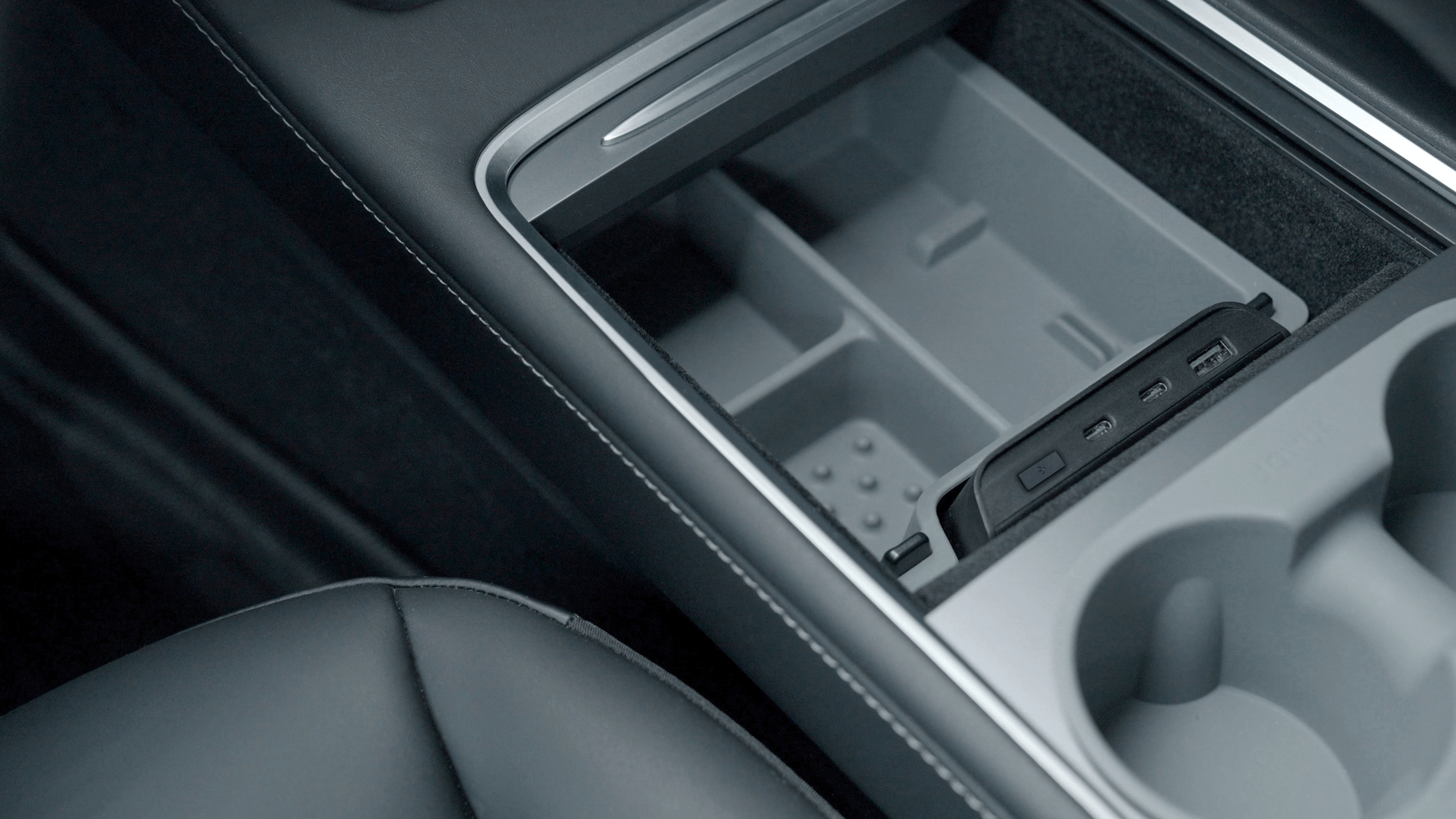 The JOWUA Center Console Tray Organizer for Tesla Model 3/Y provides a well-organized storage compartment with sections and a device charger. It features two cup holders, all crafted from premium hybrid material. This stylish accessory boasts black leather upholstery, enhancing its sleek design.