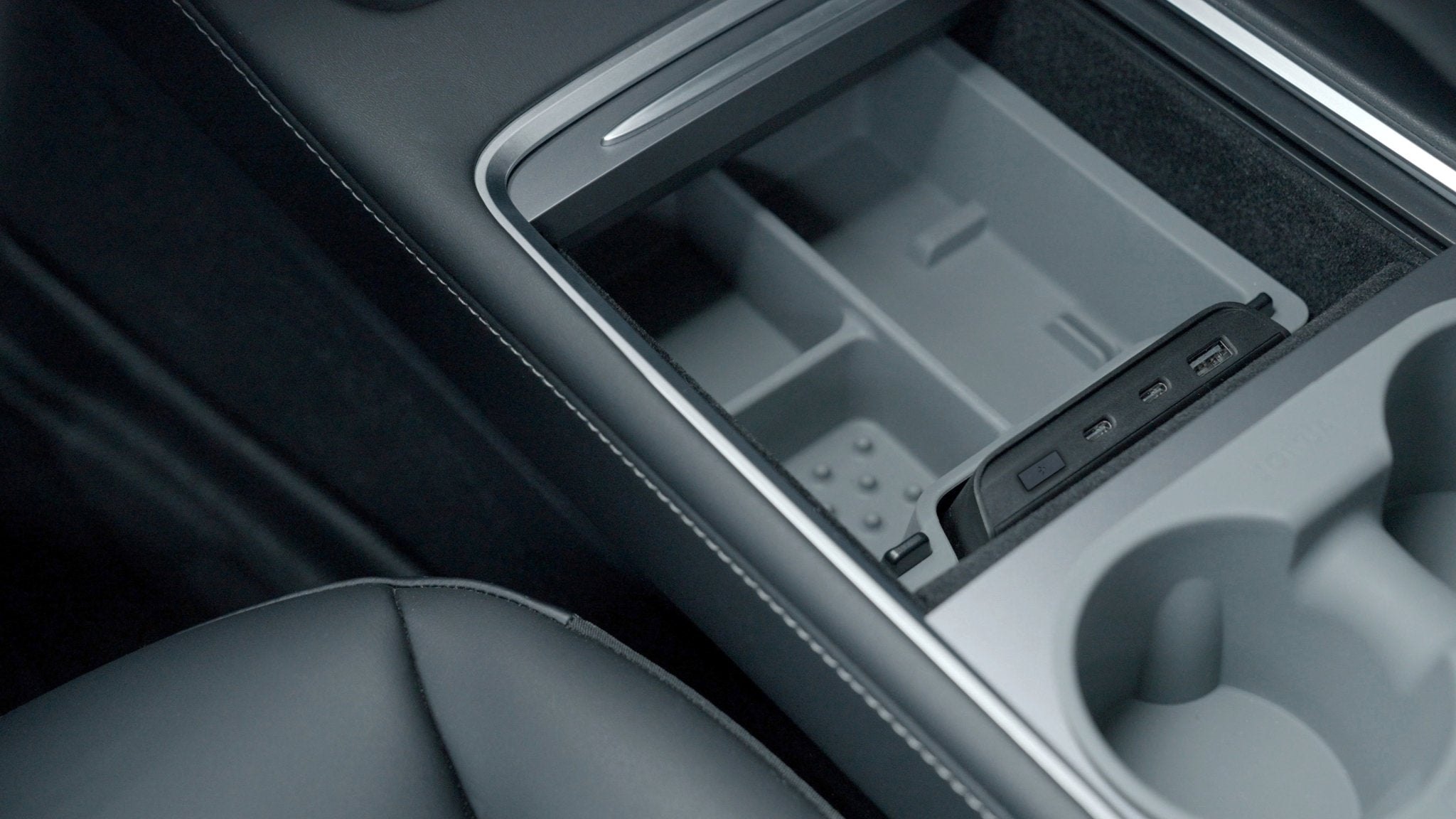 The interior design of the Tesla Model 3/Y is modern and sleek, highlighting a gray and black color scheme. Its open center console includes storage compartments, two cup holders, and a cutting-edge JOWUA USB Hub for Tesla Model 3/Y, featuring dual USB-C ports with 45W power and an LED warm light conveniently located near the driver's seat.