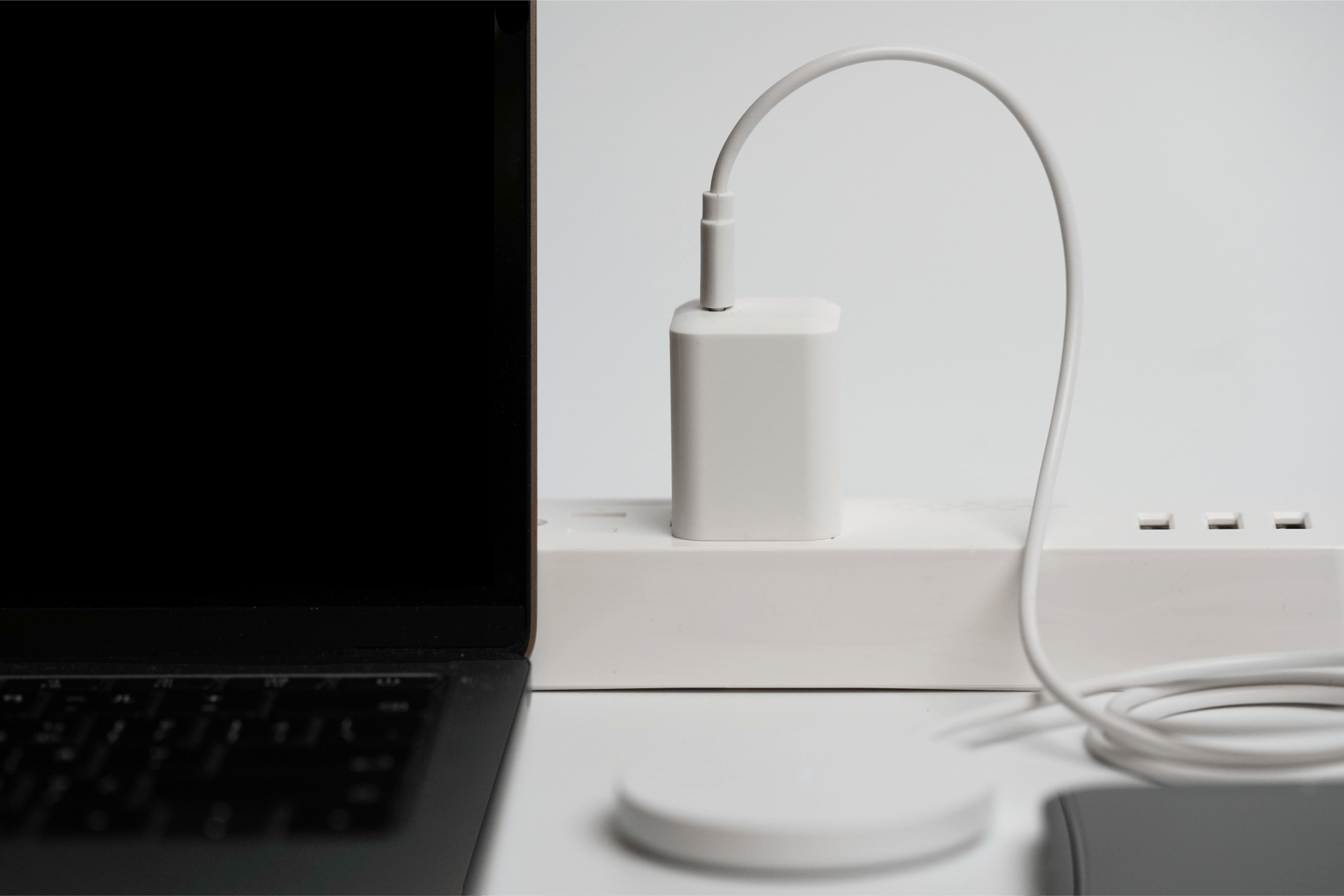 The JOWUA 100W Portable Air Compressor + Charging Solution Kit is plugged into a power strip with a coiled cable for high-speed device charging. A laptop is partially visible on the left, while a wireless charging pad lies in the foreground, ideal for tech enthusiasts.