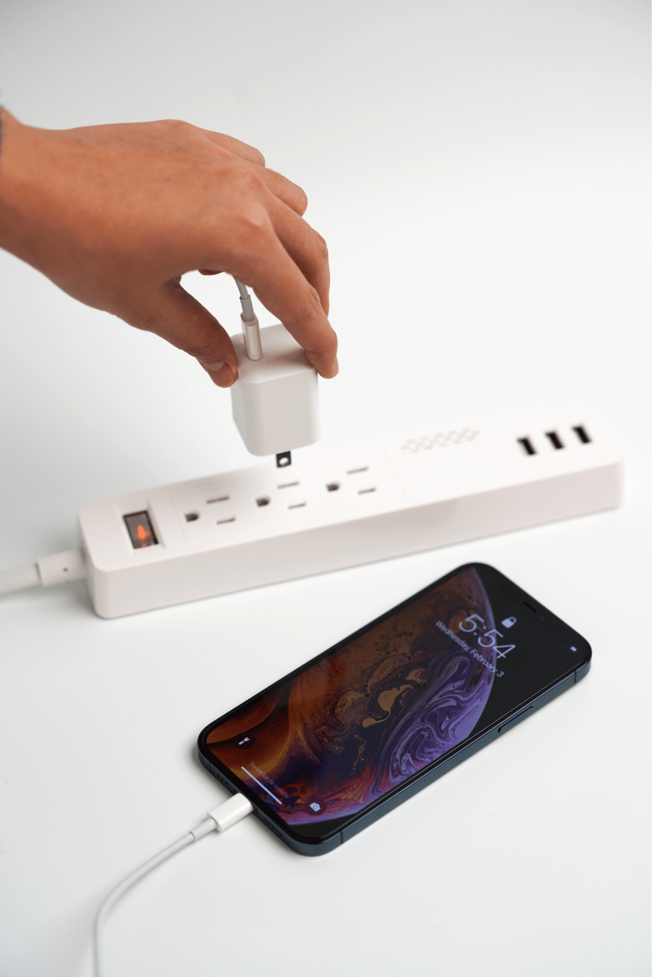 A person connects a 20W USB-C Mini Power Adapter from JOWUA, known for its sleek and compact design with multiple outlets and USB ports. Nearby, a smartphone is linked to the power adapter using a QC 3.0 charging cable, with the screen showing the time 5:54 against a plain white background.