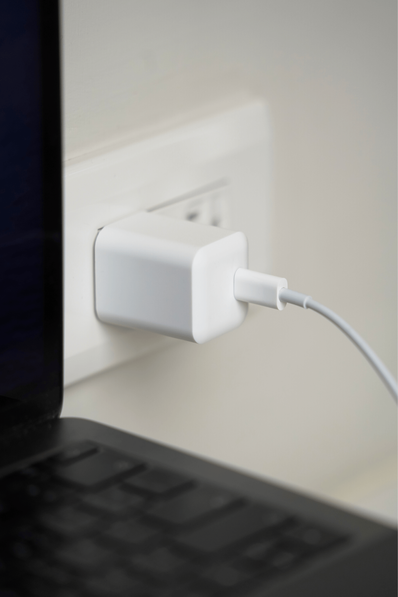 A JOWUA Portable Air Compressor + Charging Solution Kit, featuring a white charger with 60W high-speed charging capability, is plugged into a wall socket, with a cable connected to a laptop positioned on a nearby surface.