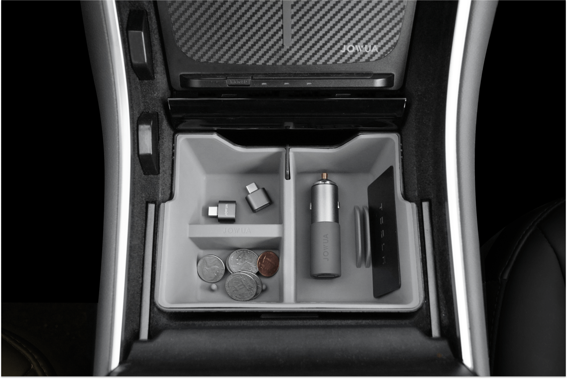 The JOWUA Center Console Tray Organizer, designed for pre-refresh Tesla Model 3 and Y, includes various compartments to securely hold coins, a small cylindrical device, USB adapters, and a card. It integrates seamlessly with Tesla accessories featuring a sleek interior design in a gray color scheme with a carbon fiber patterned cover. Constructed from premium hybrid material for enhanced durability.