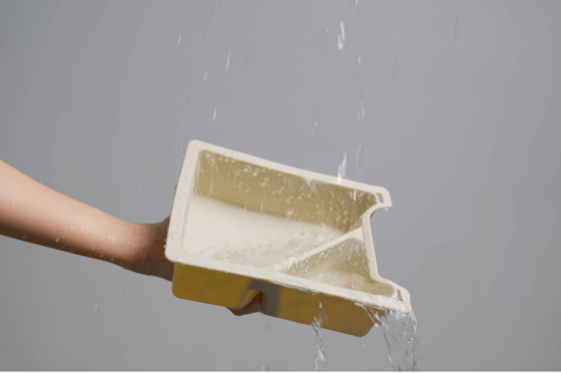 A hand holds a tilted Center Console Tray Organizer from JOWUA, designed for Tesla Model 3 / Y vehicles, crafted from premium hybrid material, with water flowing out and creating a splash against a gray background.