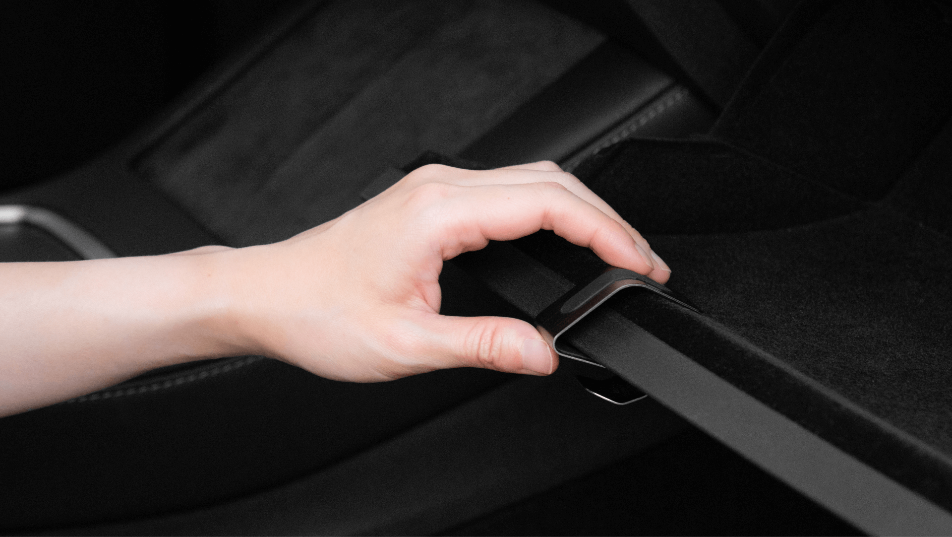 A person’s hand utilizes the Glovebox Hook for a Tesla Model 3/Y by JOWUA. The hand securely attaches the hook, preparing to organize items effortlessly. The background highlights a sleek interior with hints of stainless steel accents, showcasing modern elegance.