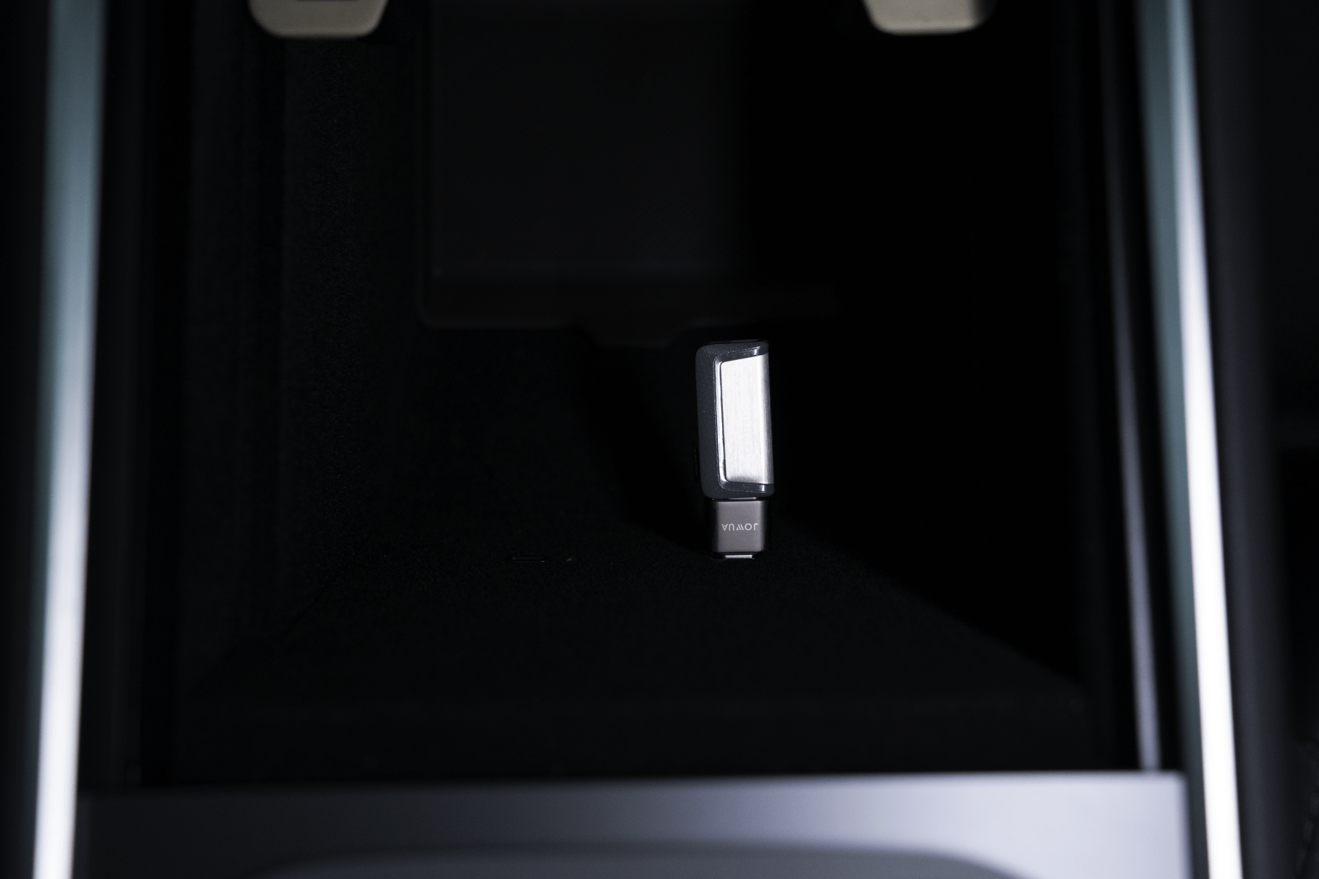 A close-up of a USB-C to USB-A Adapter(Data OTG) by JOWUA, enhanced with TeslaConnect technology, inserted into a slot within a dark compartment. The adapter has a metallic surface with "vitalBR" on its label. The compartment features metallic edges and is part of a larger electronic device.