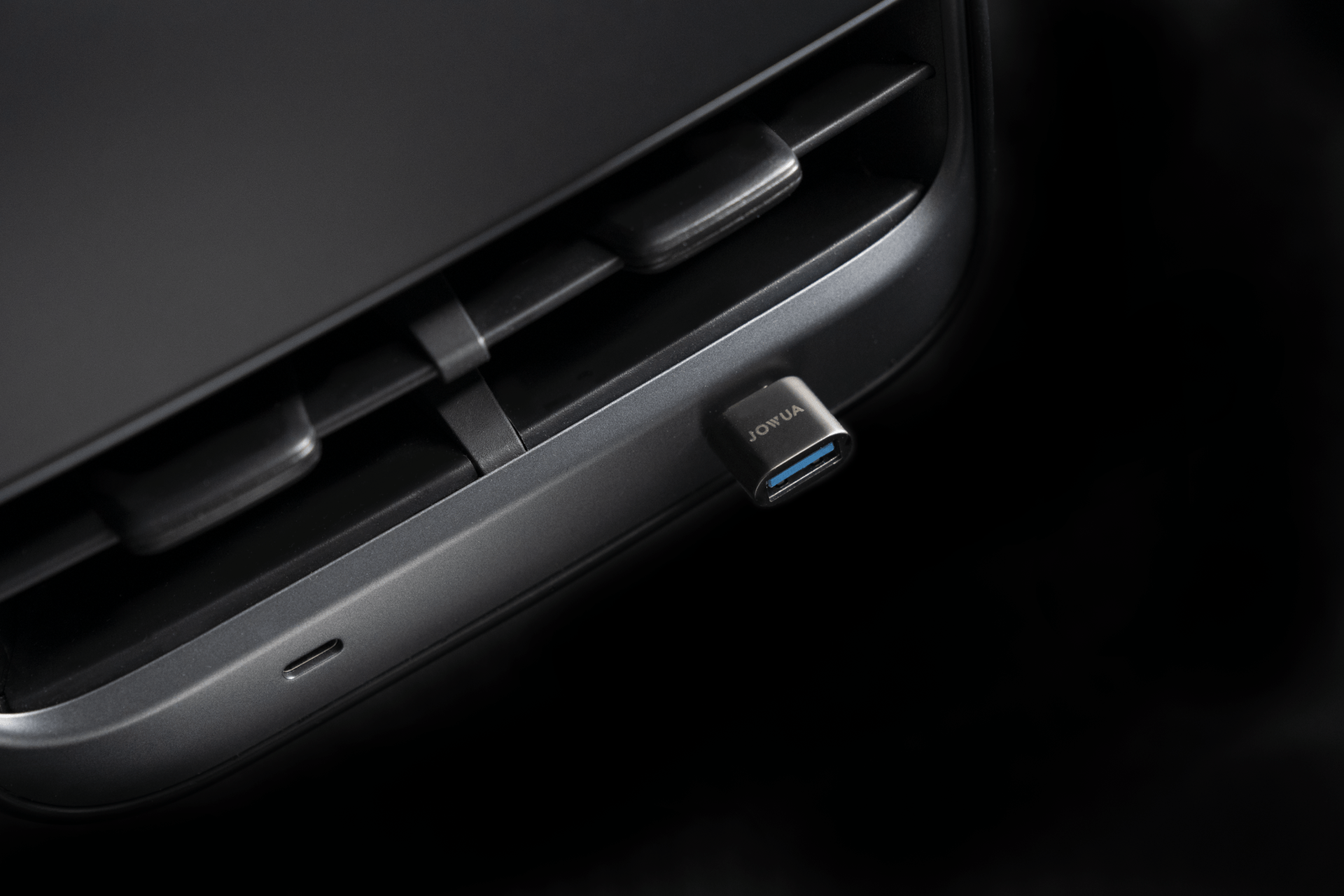 Close-up of a black USB-C to USB-A adapter plugged into a device port, set against a dark background. The adapter, perfect for data sync, proudly displays the word "JOWUA.