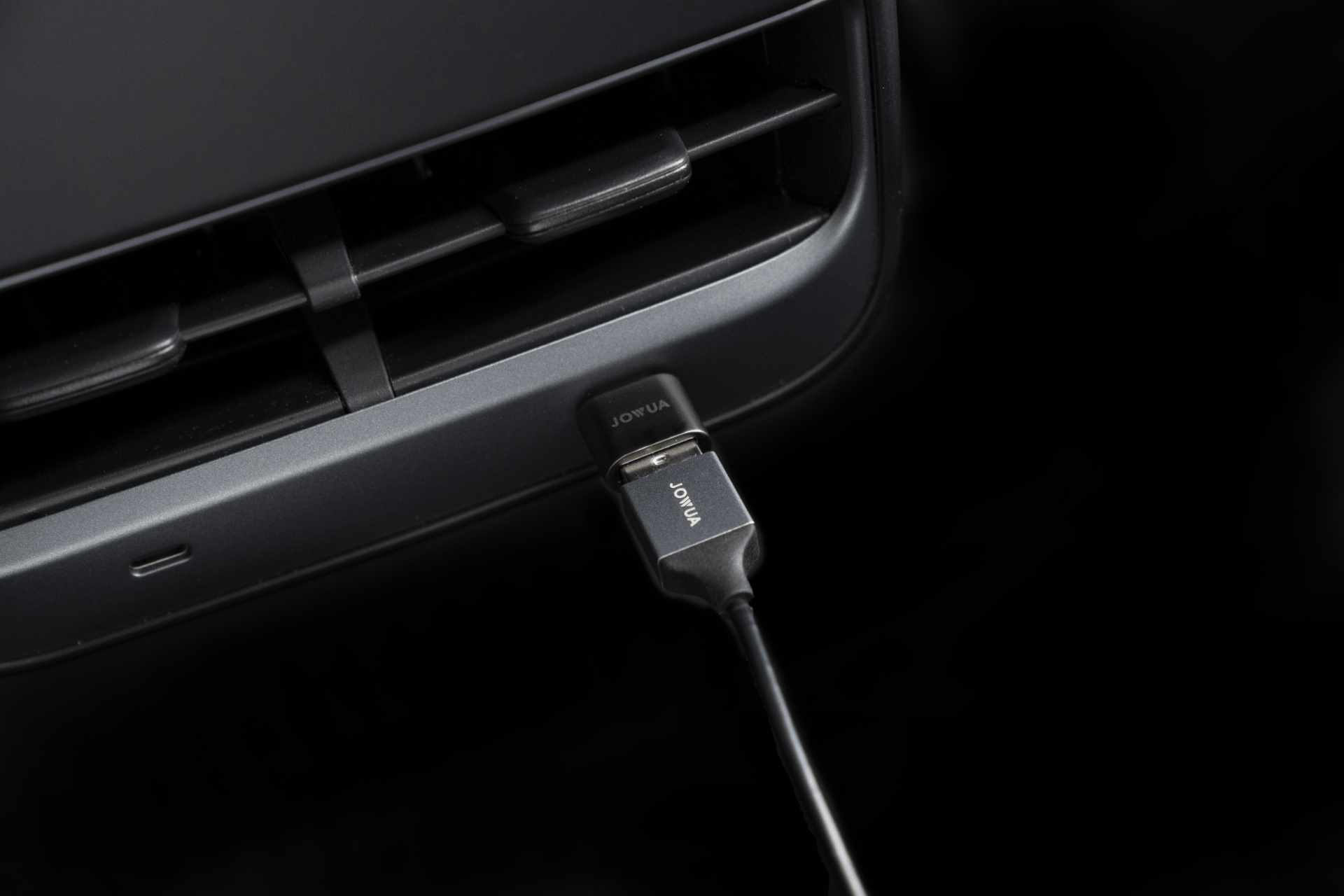 Close-up of a JOWUA USB-C to USB-A Adapter (Data OTG) connected to a USB port on a dark-colored device, with "JOWUA" visible on the plug. The surrounding area suggests it's part of an electronic device or a car dashboard, possibly hinting at TeslaConnect integration.
