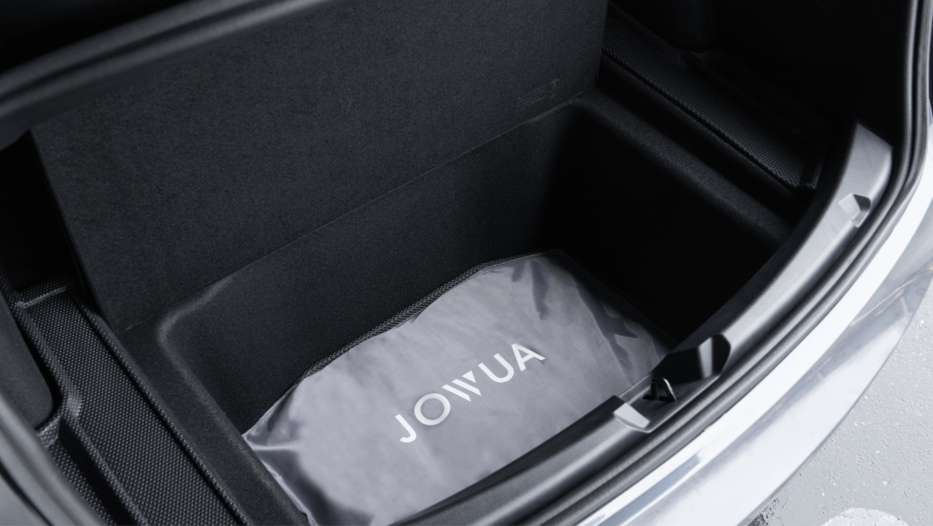 The image shows a gray "JOWUA" bag in the open front trunk (frunk) of a car. The spacious compartment has black lining, silver exterior edges, and features the Model Y (Juniper 2025+) Glass Roof Sunshade for UV protection and cooling.