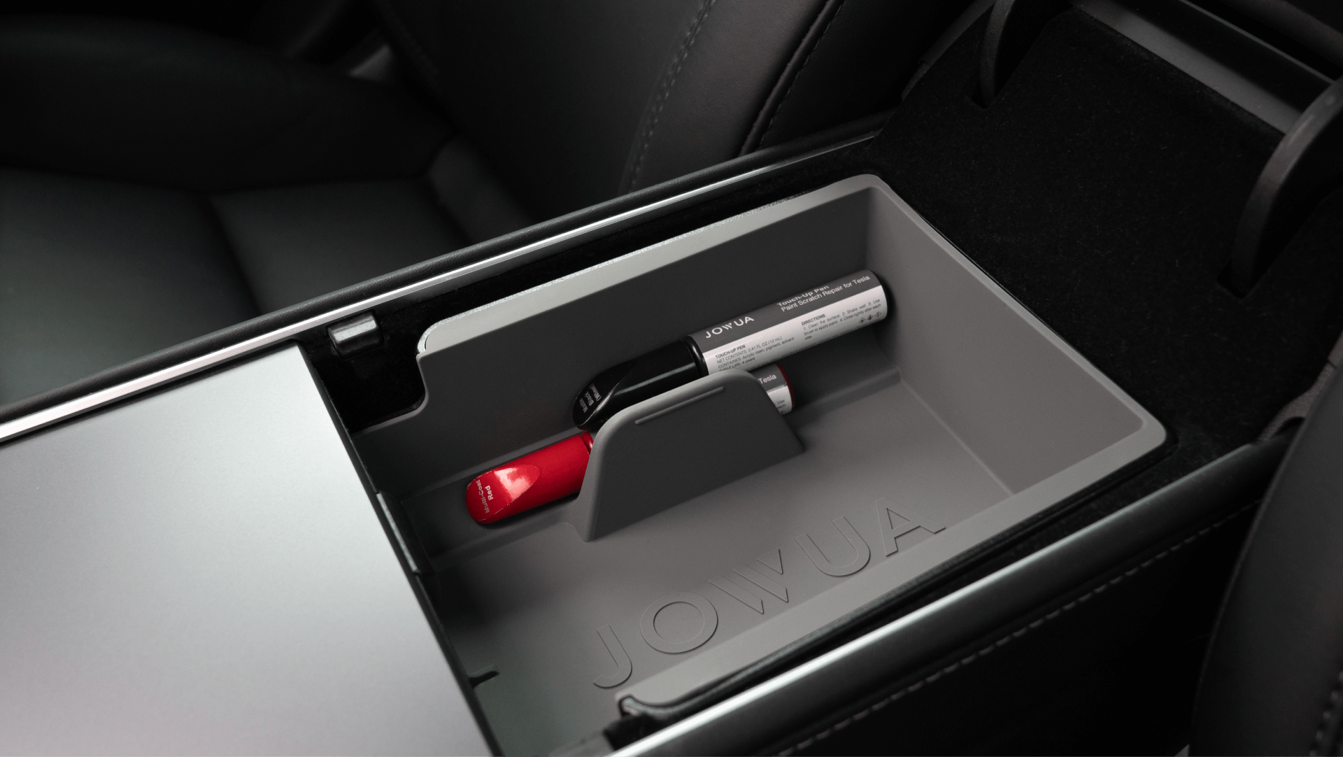 The image features the center console of a car equipped with a JOWUA organizer, complementing the sophisticated Tesla Paint look. It neatly holds a lipstick and lip balm, with the gray organizer fitting seamlessly into the compartment next to the visible car seat.